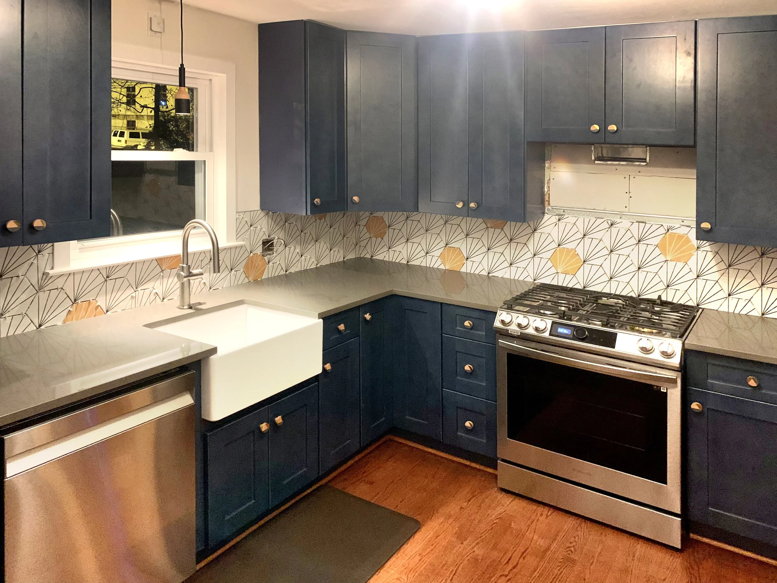 Kitchen with blue cabinets, a white farmhouse sink, a window, a stainless steel oven, and unique patterned backsplash tiles.