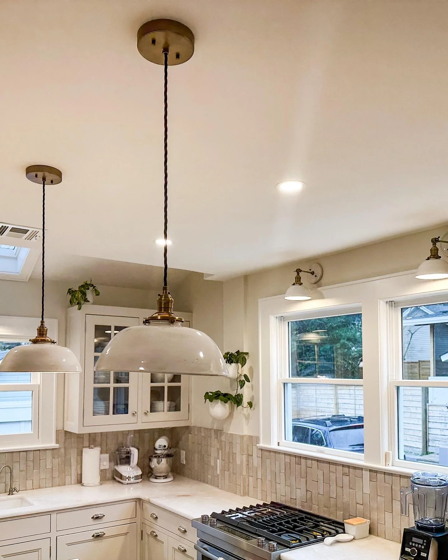 Kitchen with white cabinets, beige tiled backsplash, large windows, and two pendant lights hanging from the ceiling.