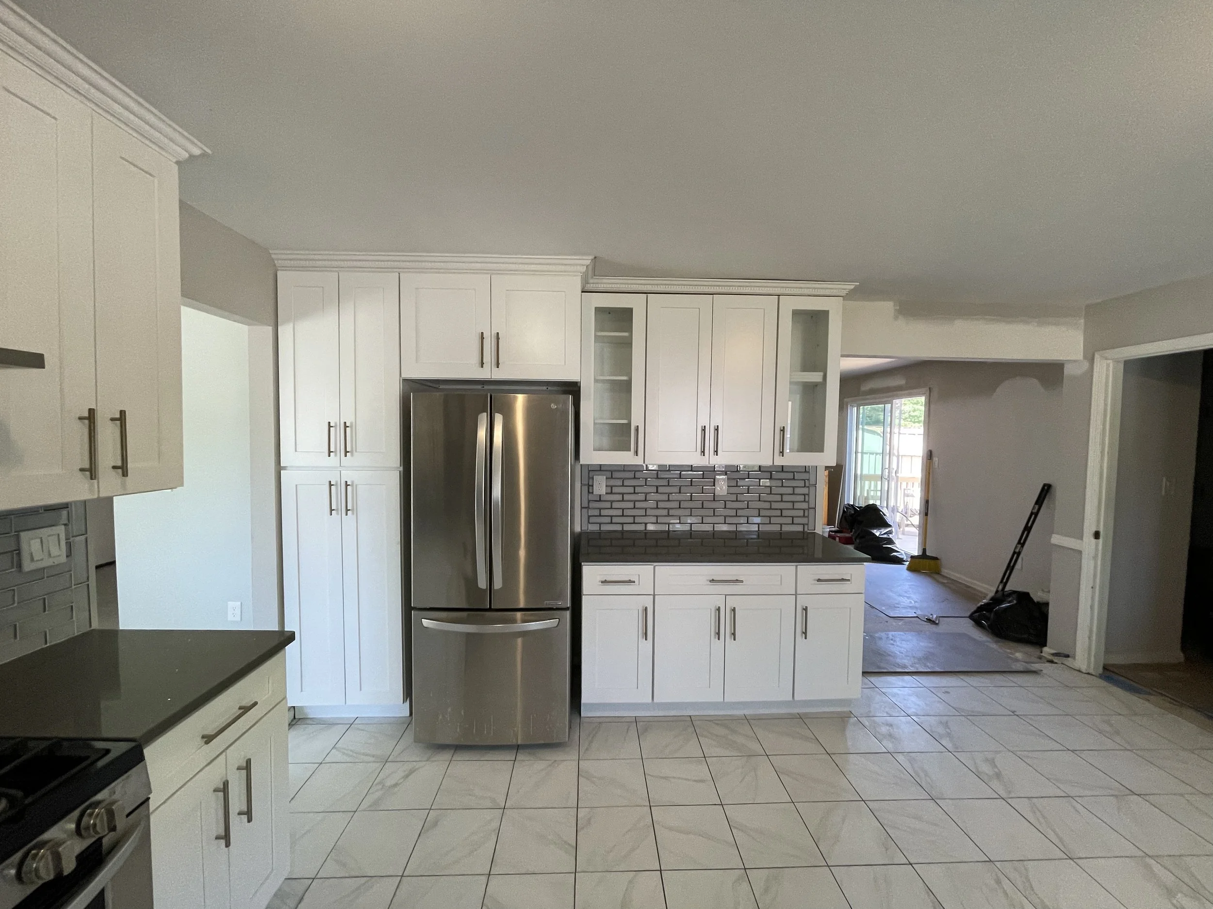 Kitchen with white cabinets, stainless steel refrigerator, tiled flooring, and gray backsplash; some construction or renovation work in progress.