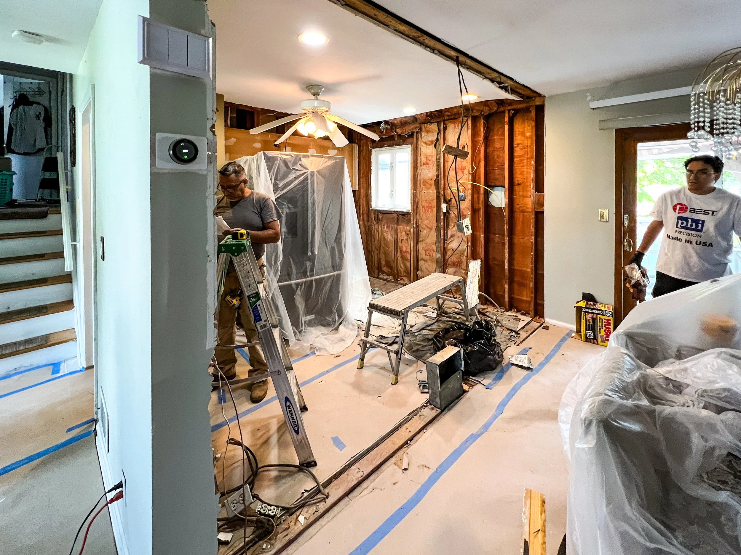 Interior remodeling with exposed wooden wall studs, construction tools, and workers.