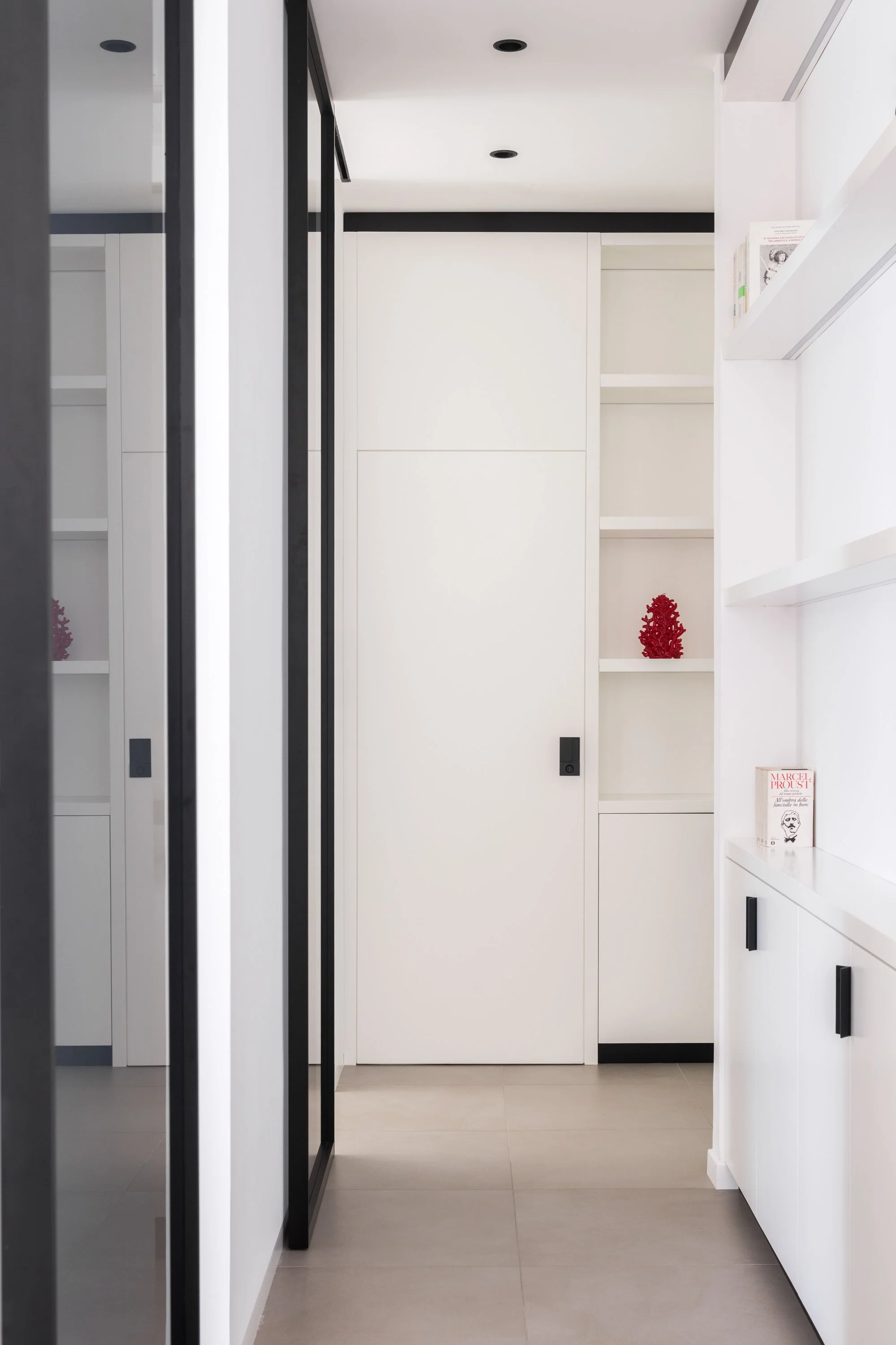 Corridoio attrezzato con falegnameria su misura in un appartamento ristrutturato a Palermo. Armadiature, librerie e porte integrate costruiscono una sequenza continua che organizza la distribuzione interna e amplifica la percezione della profondità a