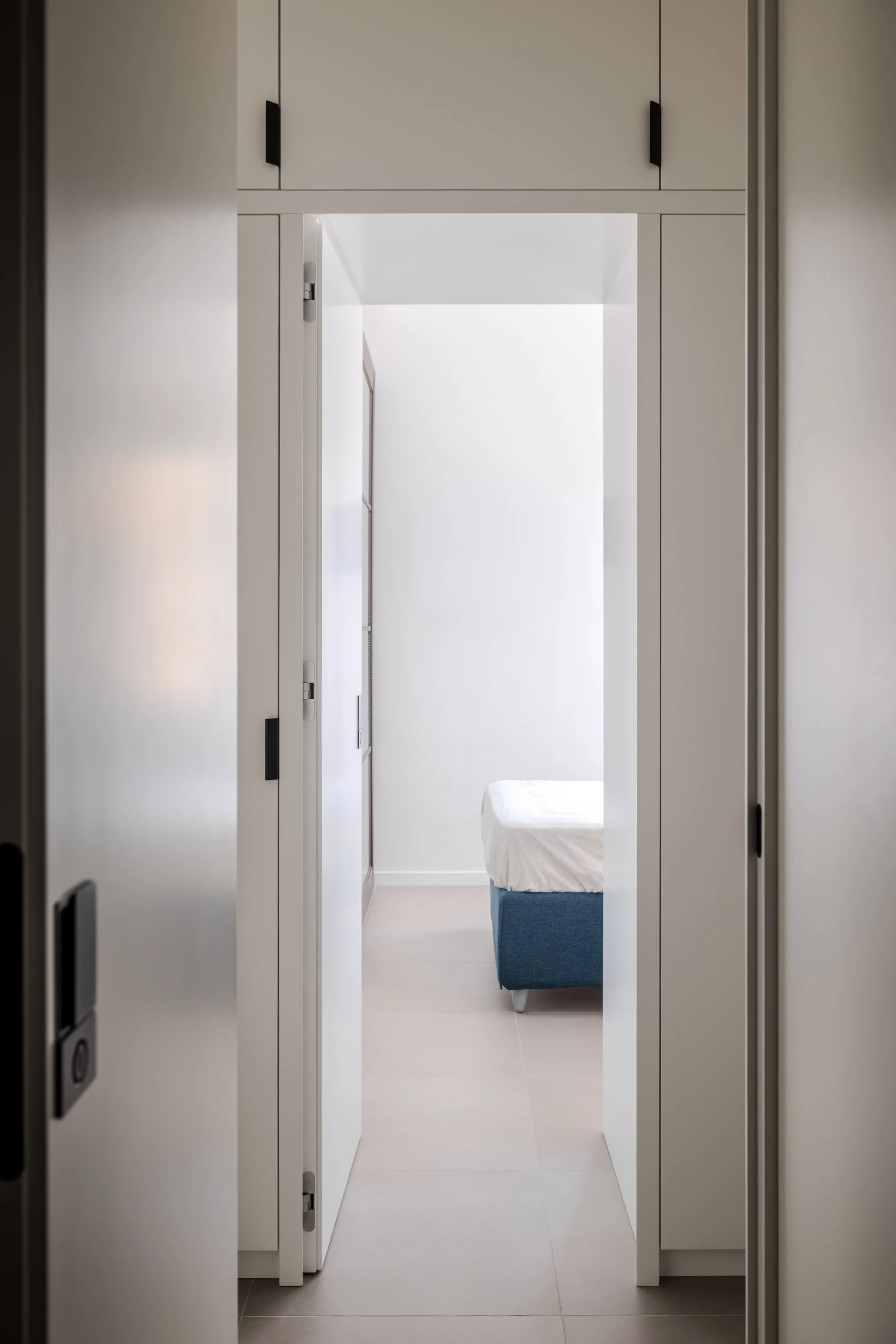 L'immagine mostra il rapporto tra contenitore e spazio servito, uno dei temi centrali del progetto. La porta aperta interrompe temporaneamente la continuità della falegnameria e rivela un ambiente raccolto, organizzato secondo criteri di essenzialità