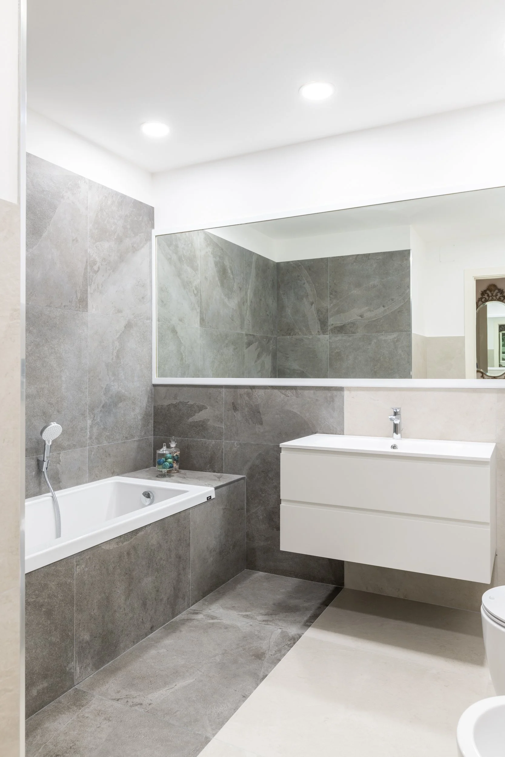 Bagno della villa ristrutturata con rivestimenti effetto pietra, vasca integrata e arredo sospeso. Il bagno combina superfici effetto pietra e arredi essenziali in una composizione equilibrata. La vasca integrata e il mobile sospeso definiscono uno s