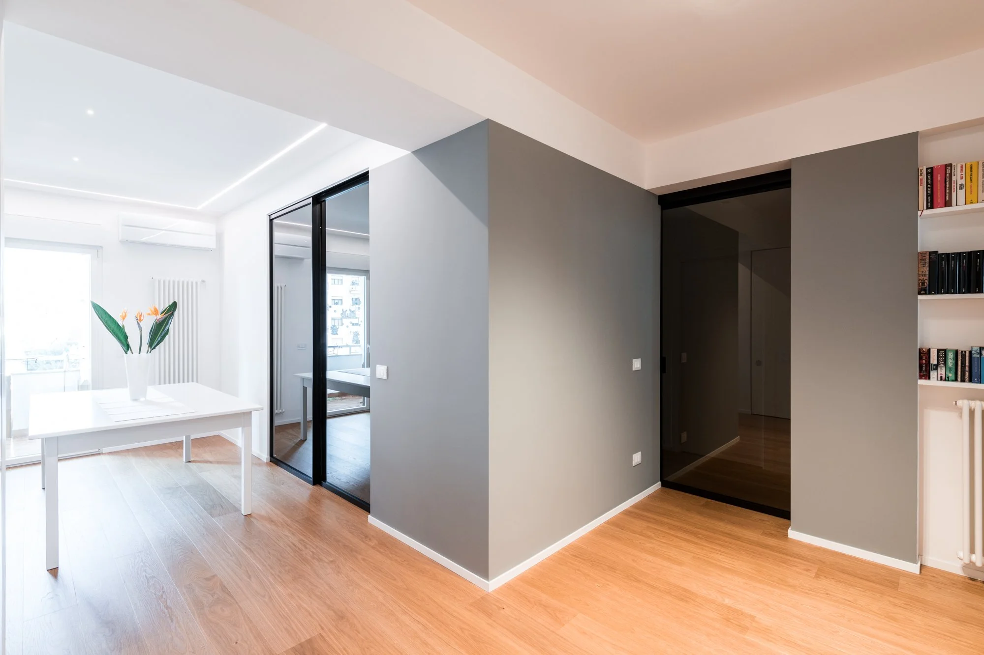 Il volume grigio centrale organizza i percorsi tra ingresso, studio, zona giorno e zona notte. La ristrutturazione dell’appartamento Mikado a Palermo ridefinisce le relazioni spaziali attraverso superfici, luce naturale, parquet in rovere e porte vet