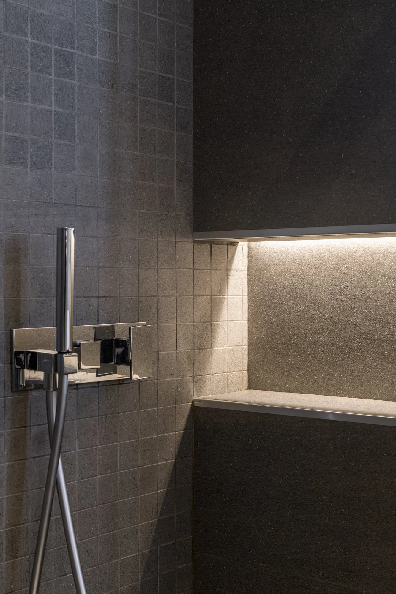 Dettaglio del bagno di servizio con rivestimento in gres effetto pietra, nicchia illuminata integrata e rubinetteria a parete. Materia, luce e texture definiscono un ambiente essenziale e contemporaneo nel progetto Mikado a Palermo.
