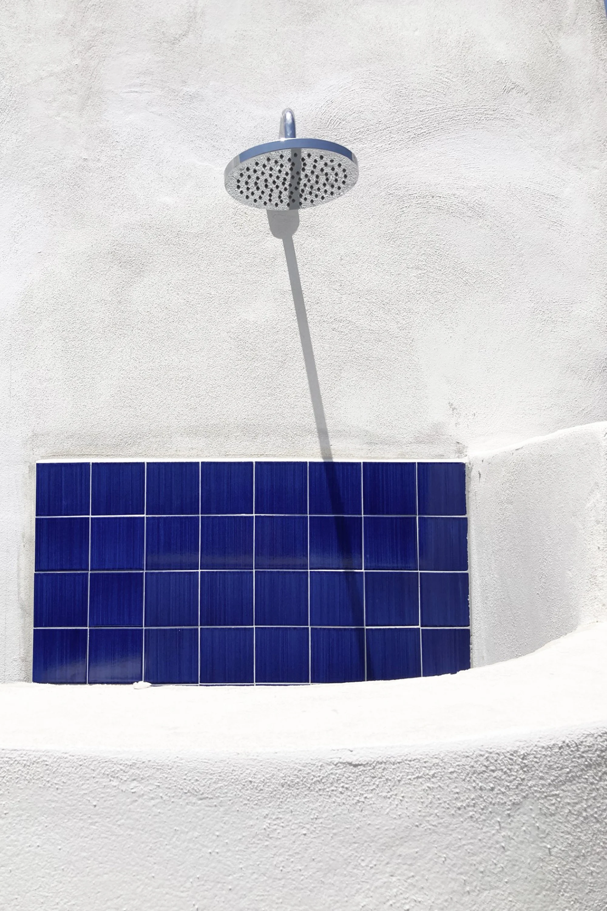 Dettaglio della doccia esterna del progetto Lithos a Pantelleria. Le superfici curve modellate nella massa muraria dialogano con il rivestimento ceramico blu ispirato ai colori del mare, reinterpretando in chiave contemporanea l’architettura del damm