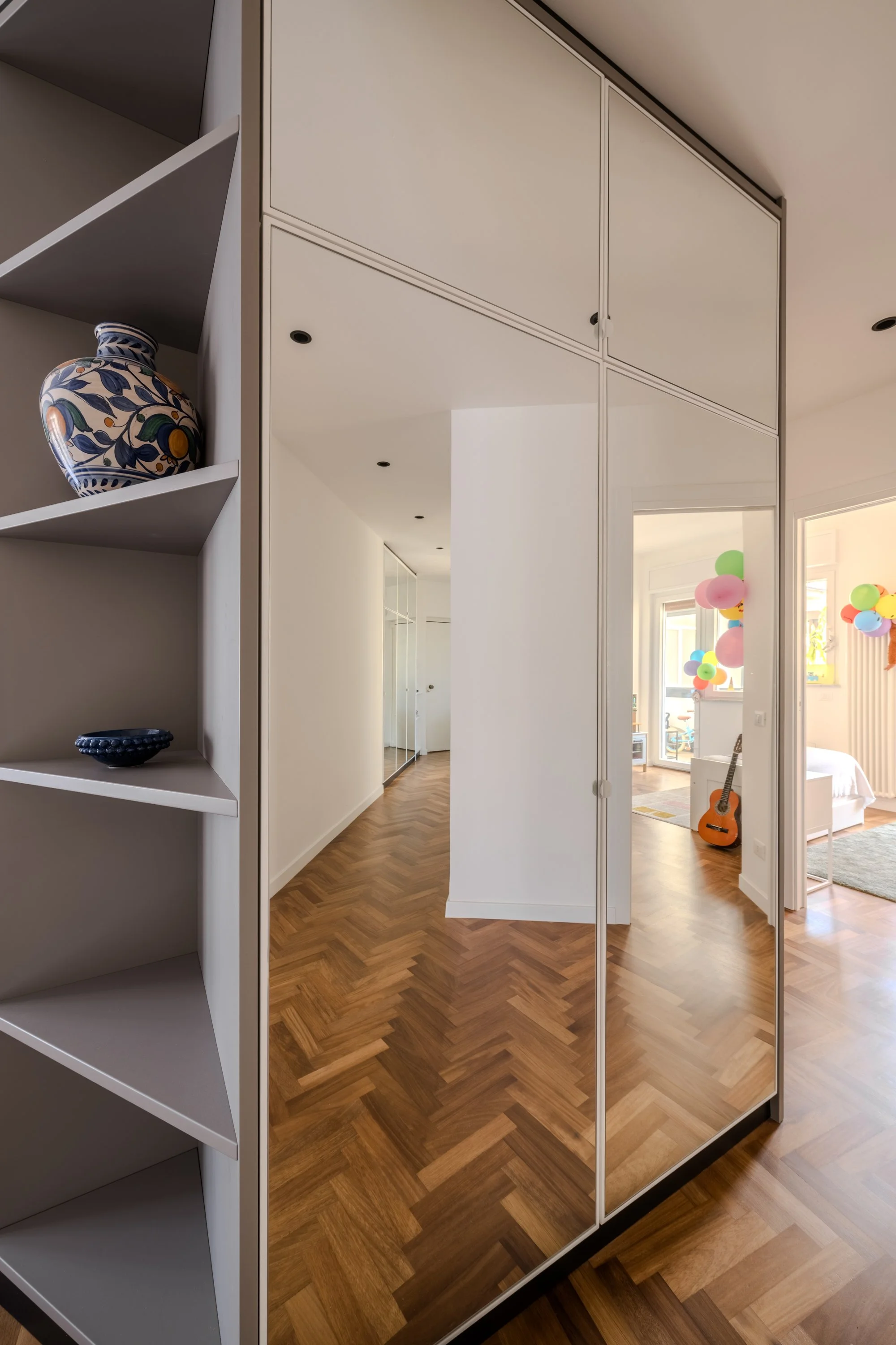 Armadiatura specchiata con libreria integrata nel disimpegno, superfici riflettenti e parquet in iroko a spina.
