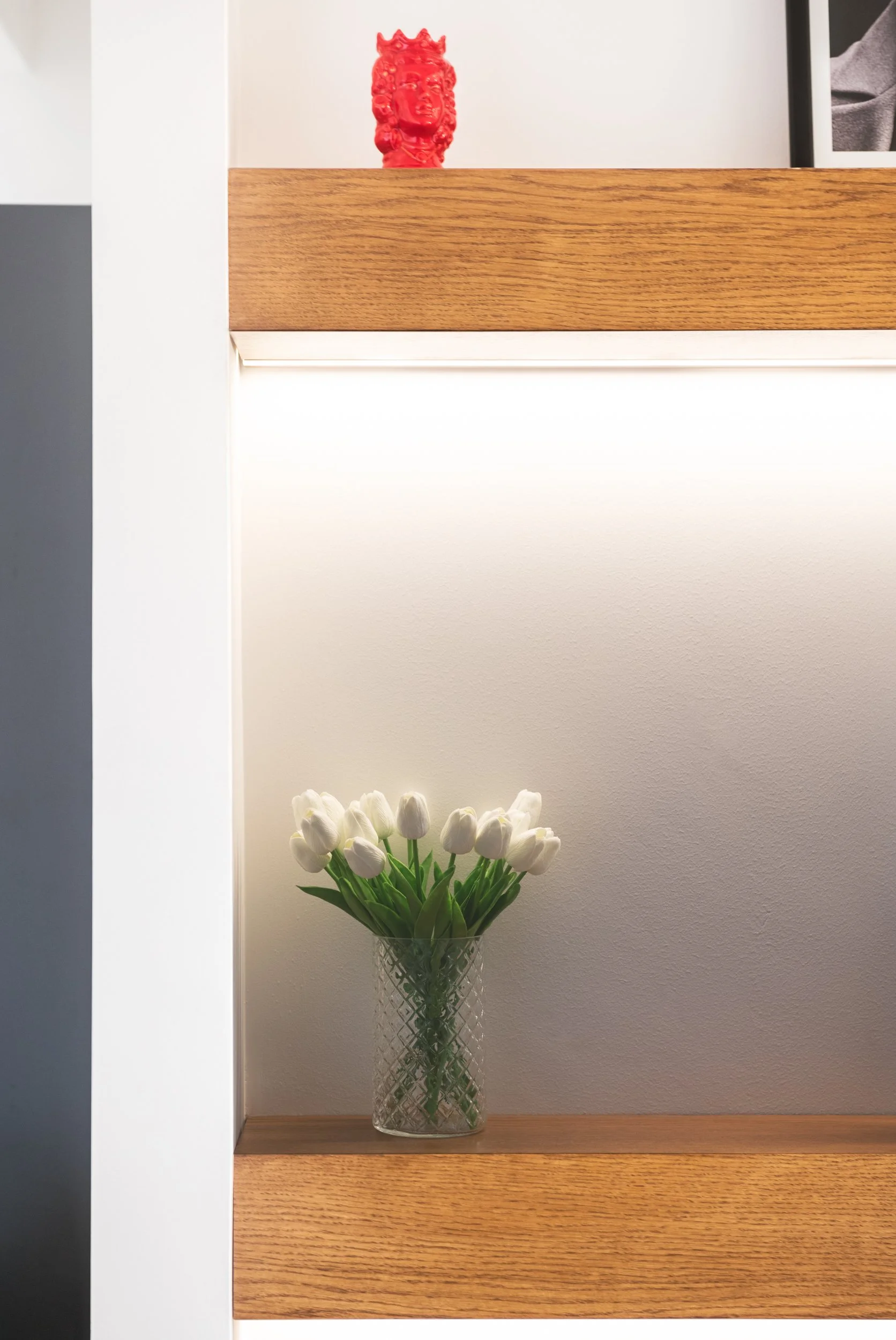 Libreria a nicchie illuminate con mensole in legno e oggetti decorativi integrata in una parete bianca di un appartamento contemporaneo a Palermo.