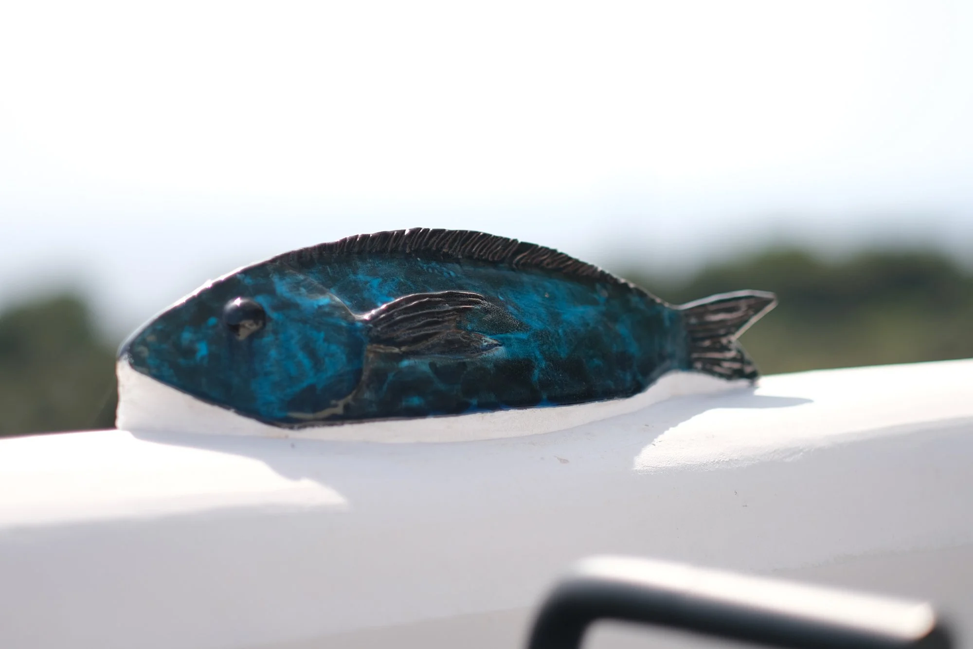Un piccolo elemento decorativo concentra l'identità del luogo in un unico gesto. La ceramica smaltata, con le sue tonalità blu profonde, richiama il mare che circonda l'isola e introduce una presenza materica capace di dialogare con la luce intensa d