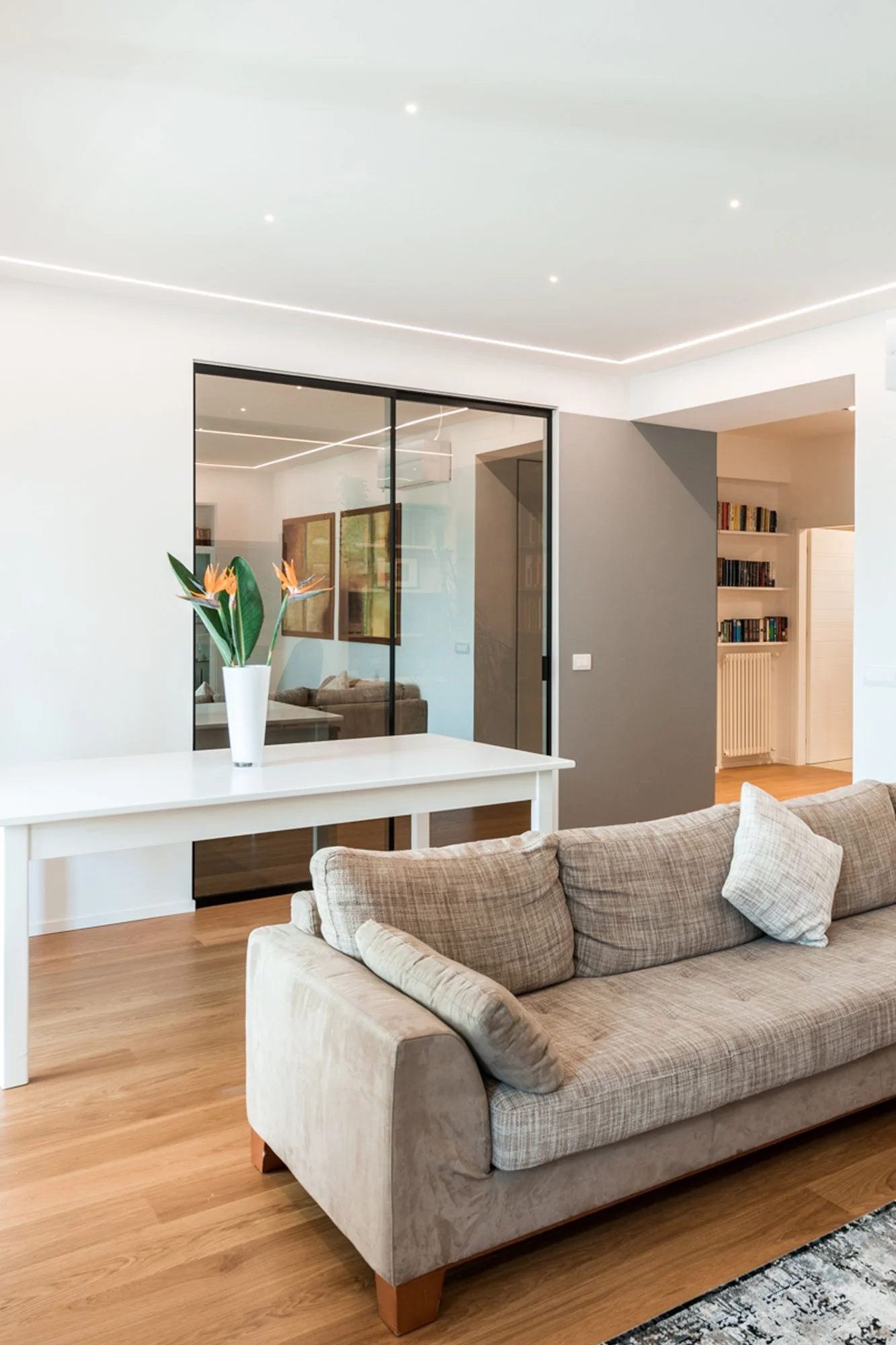 Le porte vetrate fumé definiscono il rapporto tra soggiorno e studio mantenendo continuità visiva e luminosità naturale. Un progetto di interior design a Palermo caratterizzato da equilibrio compositivo, superfici neutre e materiali contemporanei.
