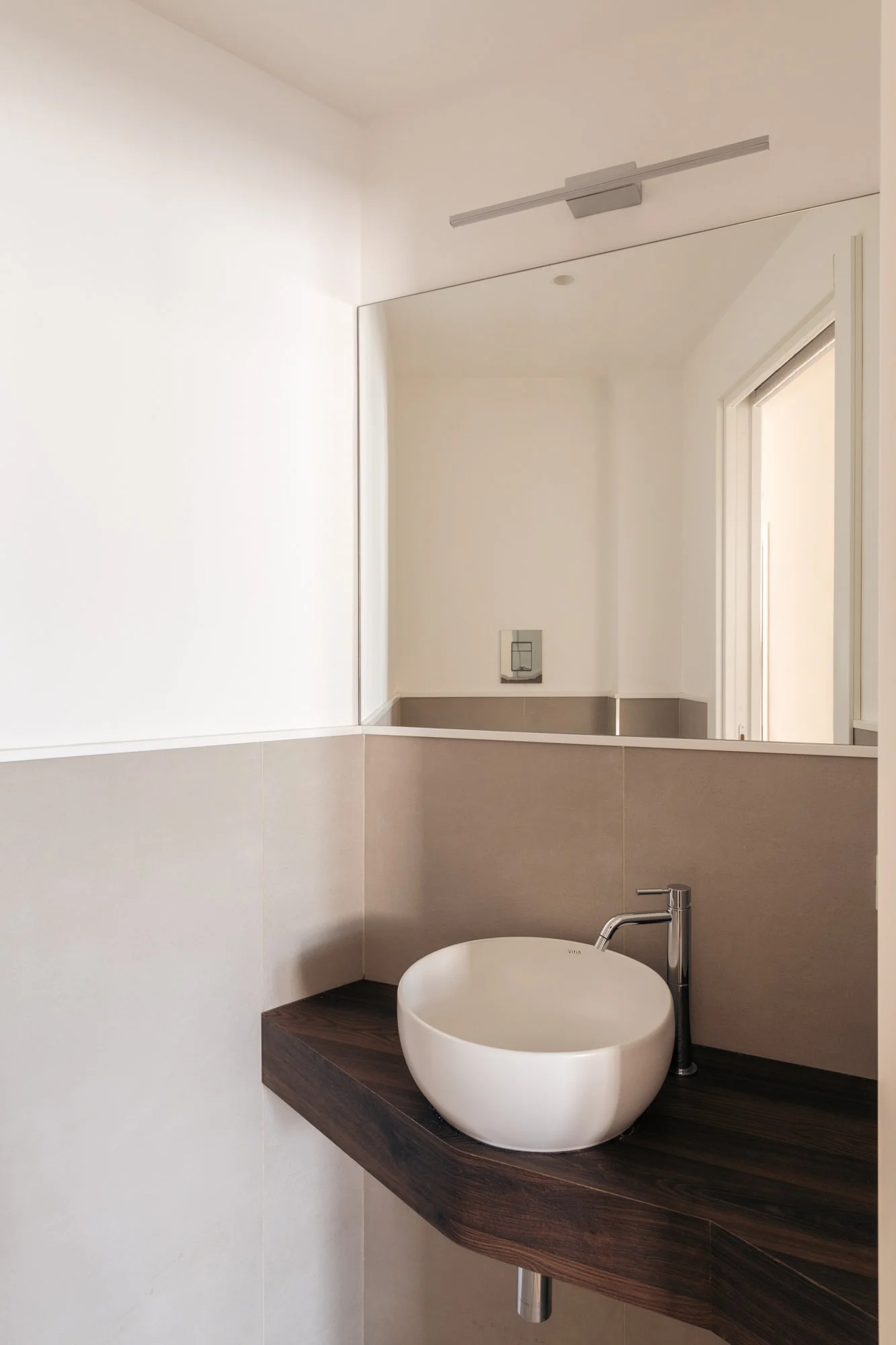 Bagno minimale e contemporaneo con piano di appoggio in effetto legno e ciotola circolare.