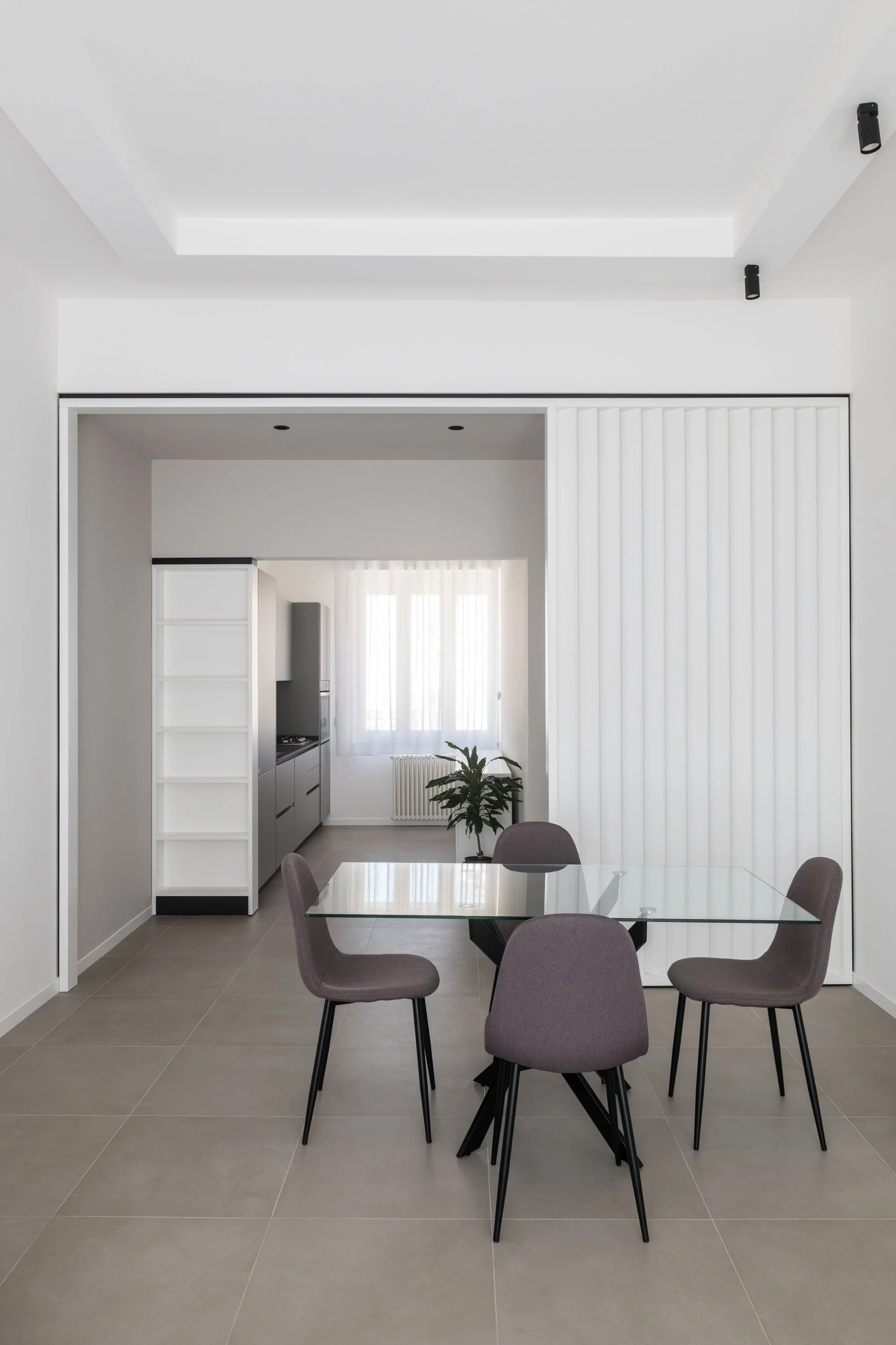 Il brise-soleil laccato bianco definisce una soglia permeabile tra zona pranzo e cucina. L’elemento filtra le visuali, mantiene la continuità spaziale e diventa il dispositivo che connette i diversi ambienti dell’appartamento Ink a Palermo.