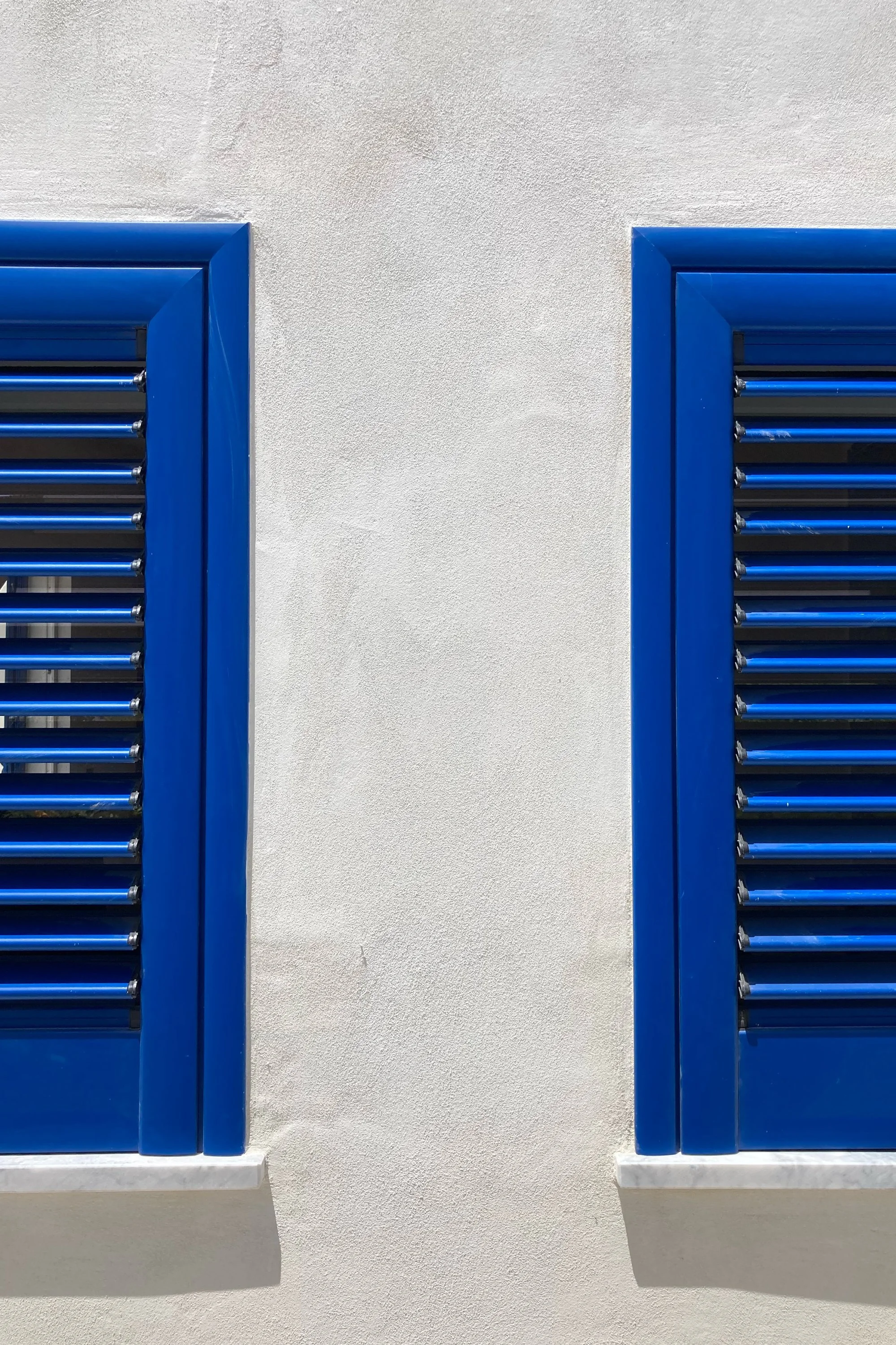 Finestre blu in dammuso ristrutturato a Pantelleria con pareti bianche e architettura mediterranea contemporanea.