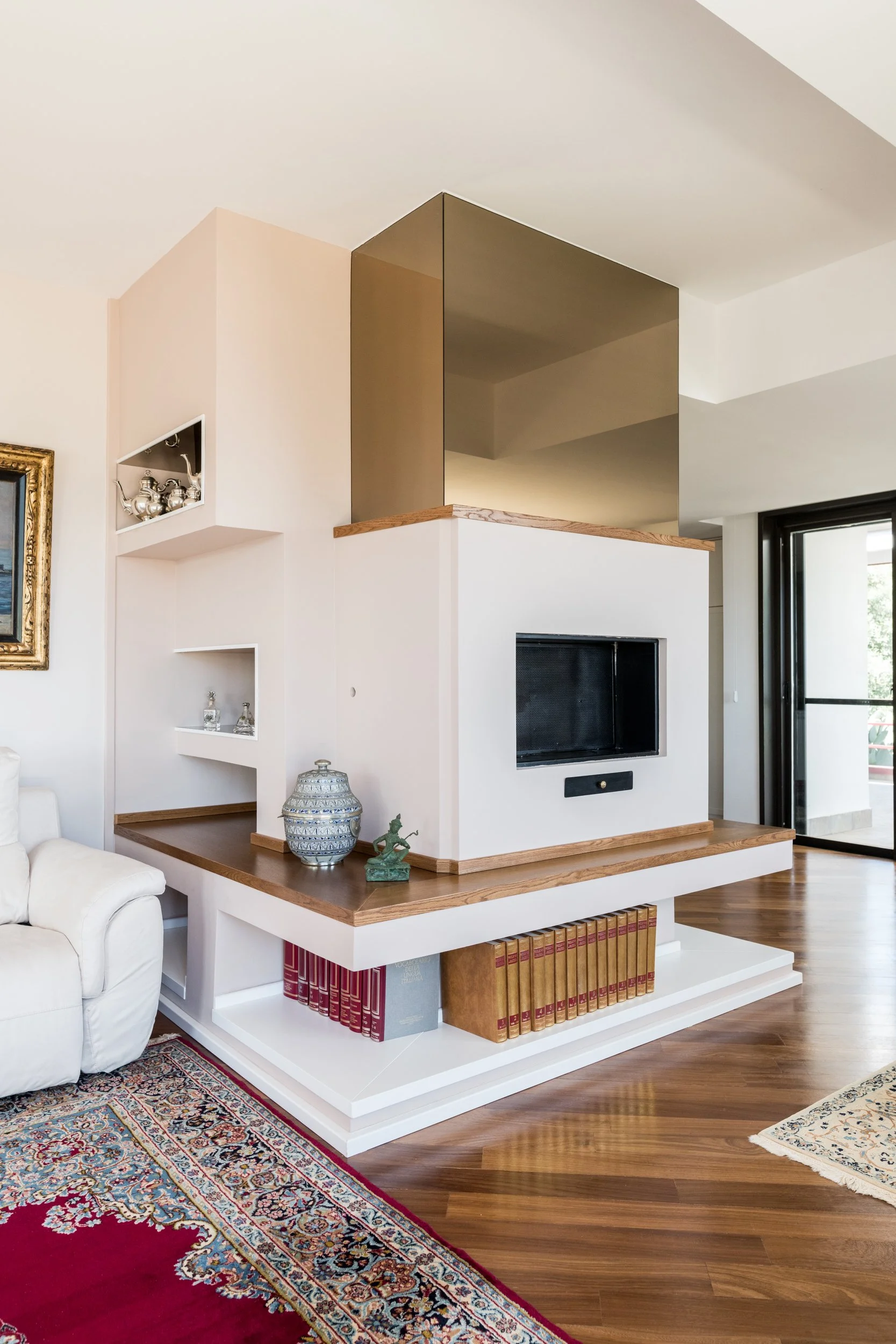 Camino centrale progettato come elemento d'arredo su misura nella zona giorno della villa. Il camino centrale organizza lo spazio giorno diventando elemento architettonico e funzionale. Le superfici laccate, gli inserti in legno e i vani espositivi d