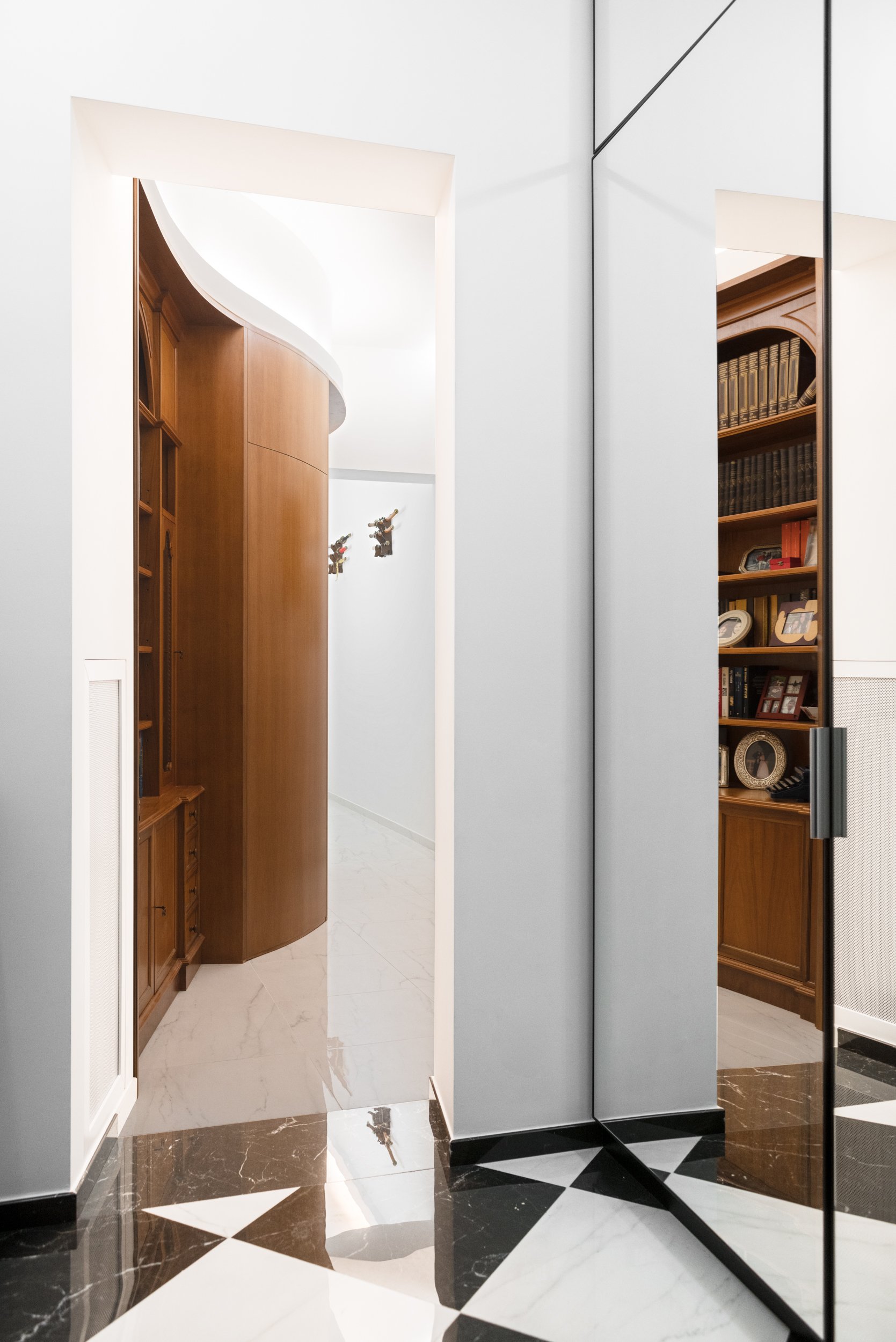 Ingresso di appartamento ristrutturato a Palermo con pavimento geometrico effetto marmo, armadio riflettente, libreria su misura e corridoio curvo realizzato attraverso falegnameria integrata.