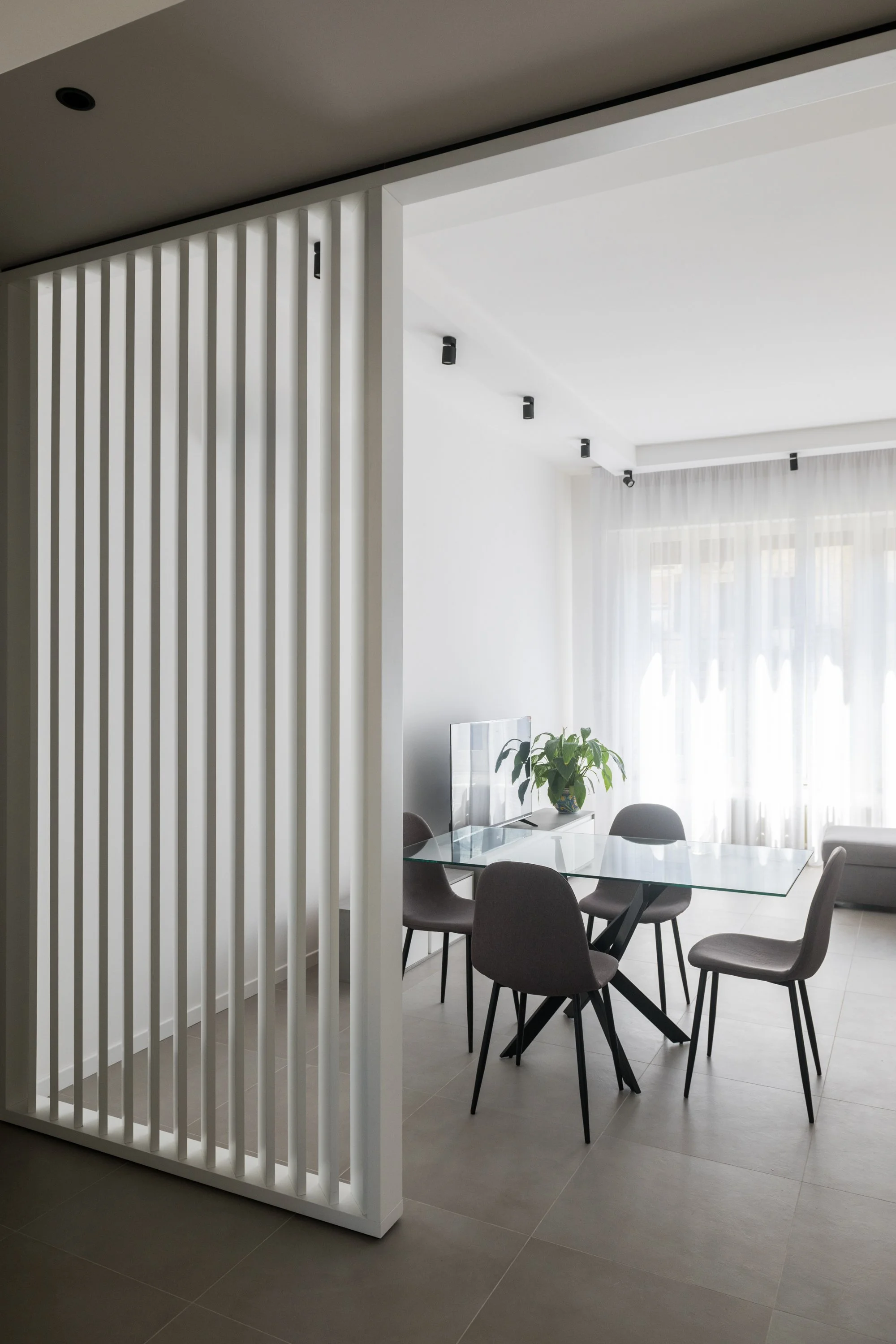 Il brise-soleil laccato bianco definisce una soglia permeabile tra zona pranzo e cucina. L’elemento filtra le visuali, mantiene la continuità spaziale e diventa il dispositivo che connette i diversi ambienti dell’appartamento Ink a Palermo.