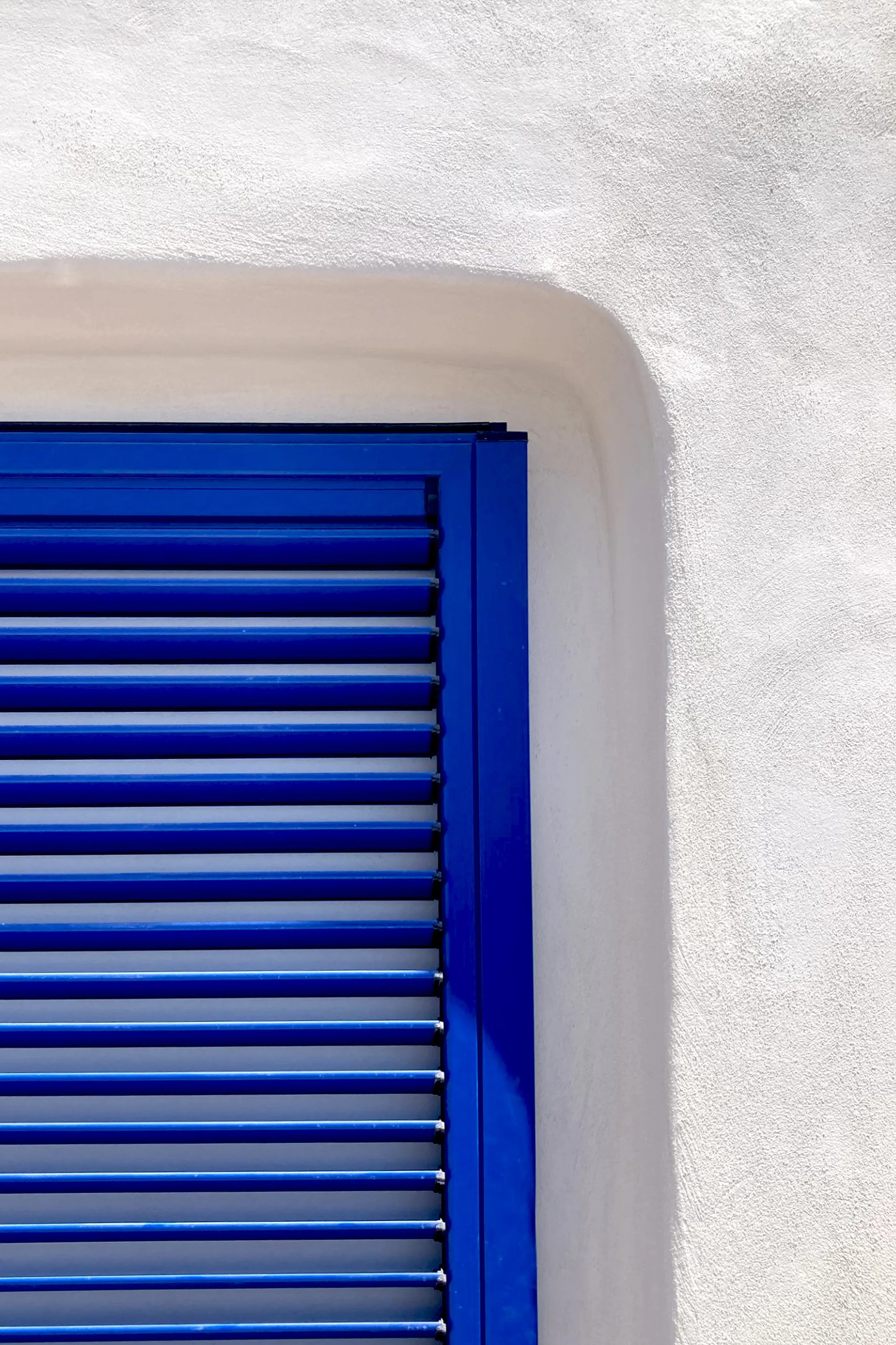 Dettaglio di finestra blu inserita in una parete curva di dammuso ristrutturato a Pantelleria.