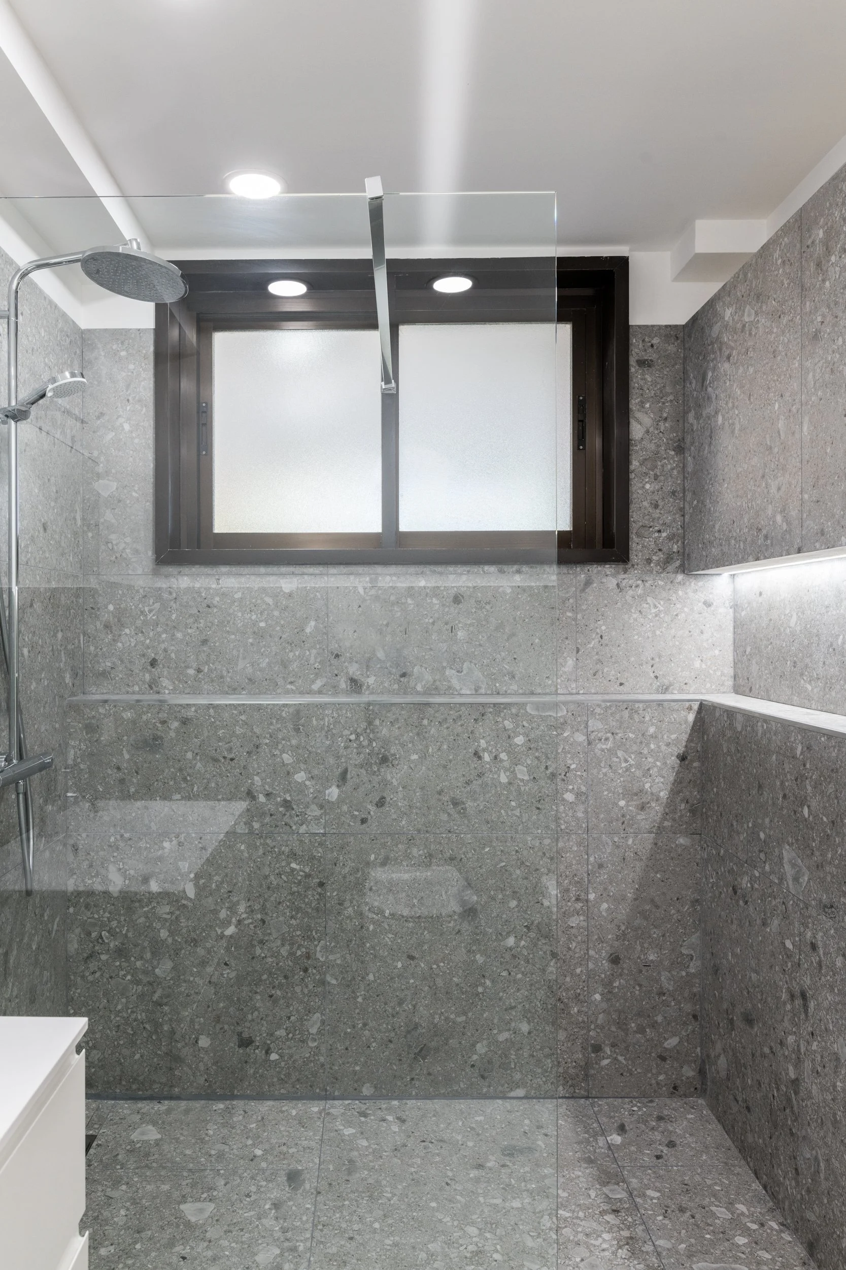Vista della doccia walk-in con illuminazione integrata e rivestimenti lapidei nella villa a Palermo. L'ambiente bagno è caratterizzato da rivestimenti lapidei, luce integrata e dettagli minimali. Le superfici continue amplificano la percezione dello 