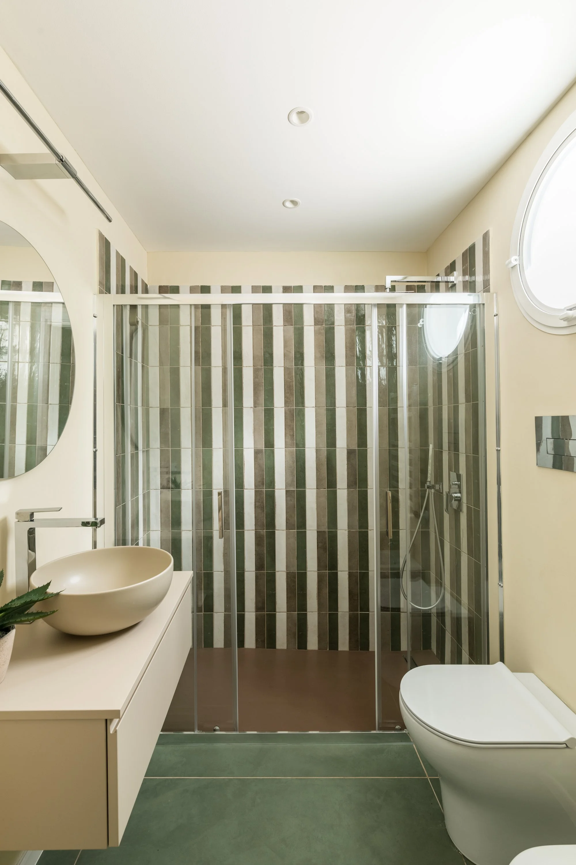 Bagno contemporaneo a Mondello con rivestimento in piastrelle verticali verdi, beige e bianche, box doccia in vetro e lavabo freestanding. Il progetto di Francesco Di Raimondo combina una palette naturale con pavimento verde, superfici chiare e detta