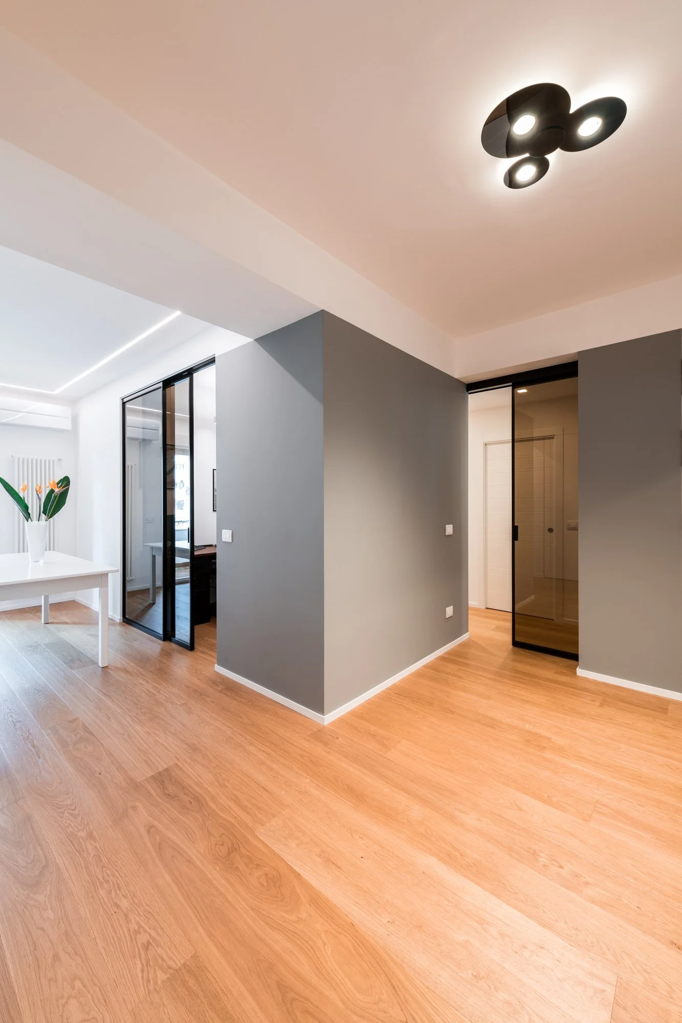 Il volume grigio centrale organizza i percorsi tra ingresso, studio, zona giorno e zona notte. La ristrutturazione dell’appartamento Mikado a Palermo ridefinisce le relazioni spaziali attraverso superfici, luce naturale, parquet in rovere e porte vet