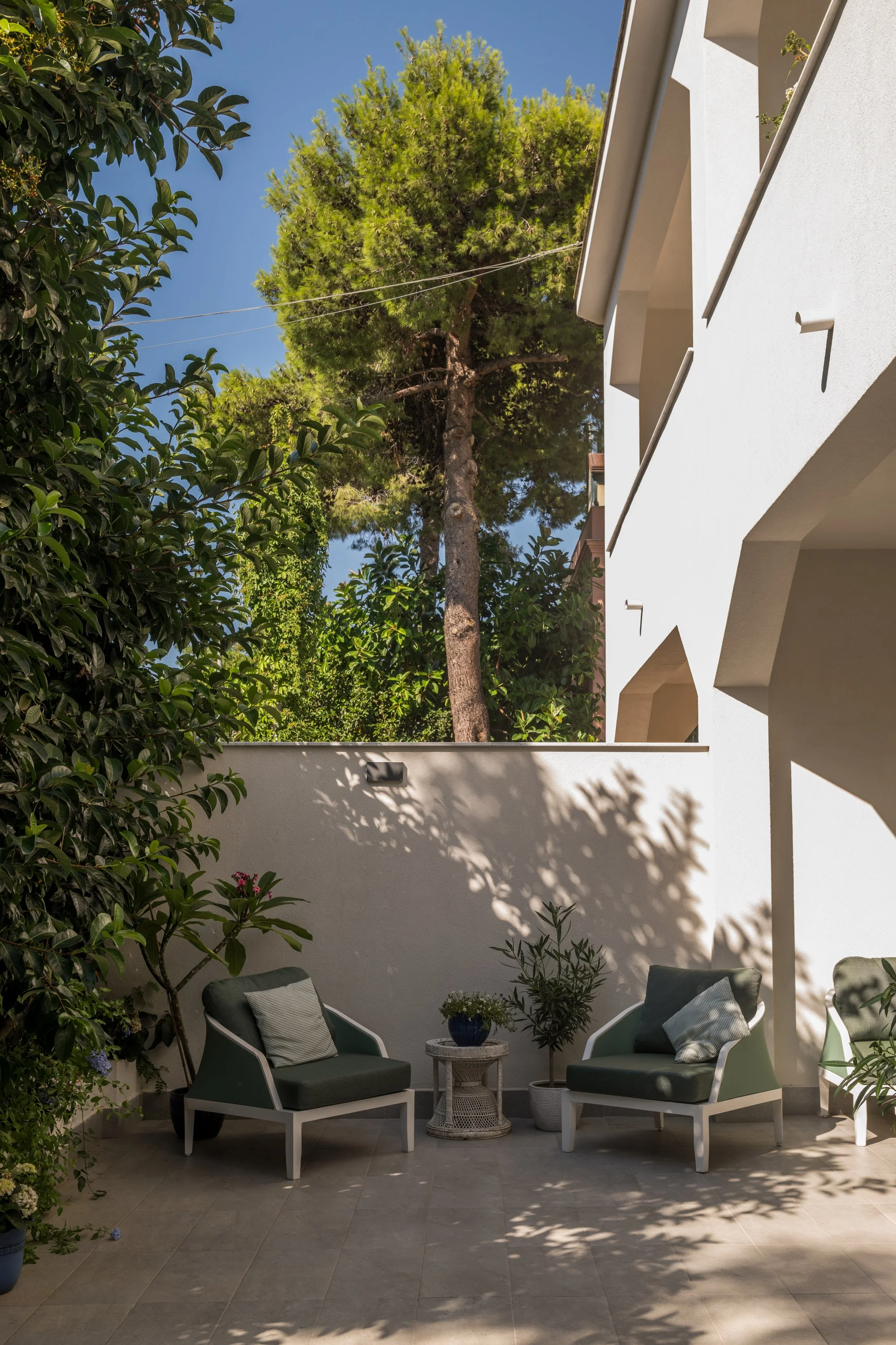 Terrazza esterna della villa a Mondello, Palermo, trasformata attraverso un progetto integrato di architettura e interior design.. La zona relax all'aperto è organizzata tra pavimentazione effetto pietra, arredi, vegetazione mediterranea e pareti bia