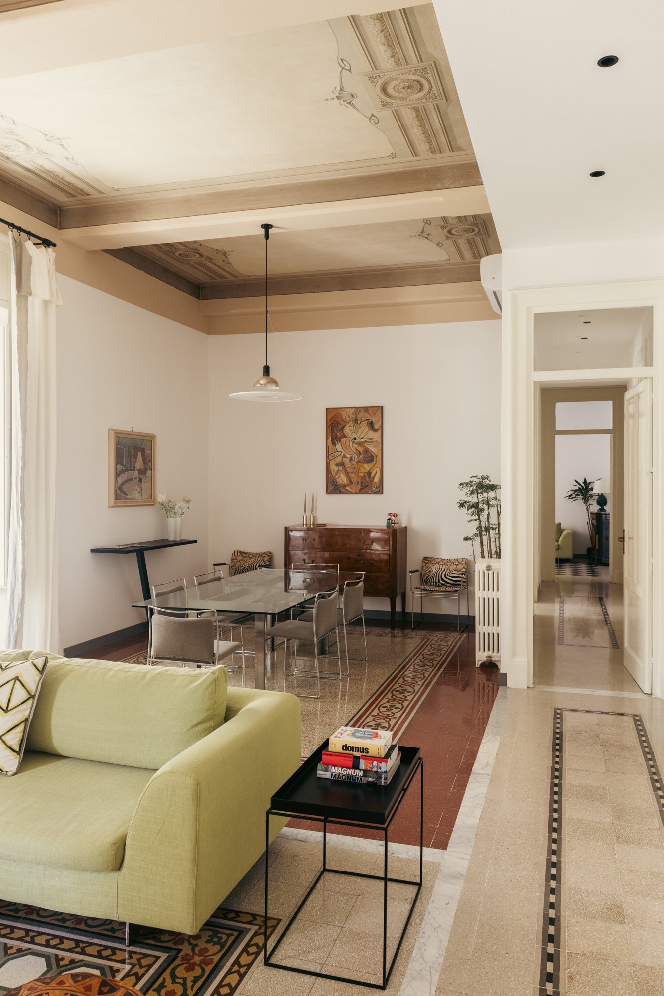 Soffitti decorati, pavimenti storici e arredi contemporanei definiscono la zona giorno di questo appartamento restaurato a Palermo, in equilibrio tra conservazione e trasformazione.