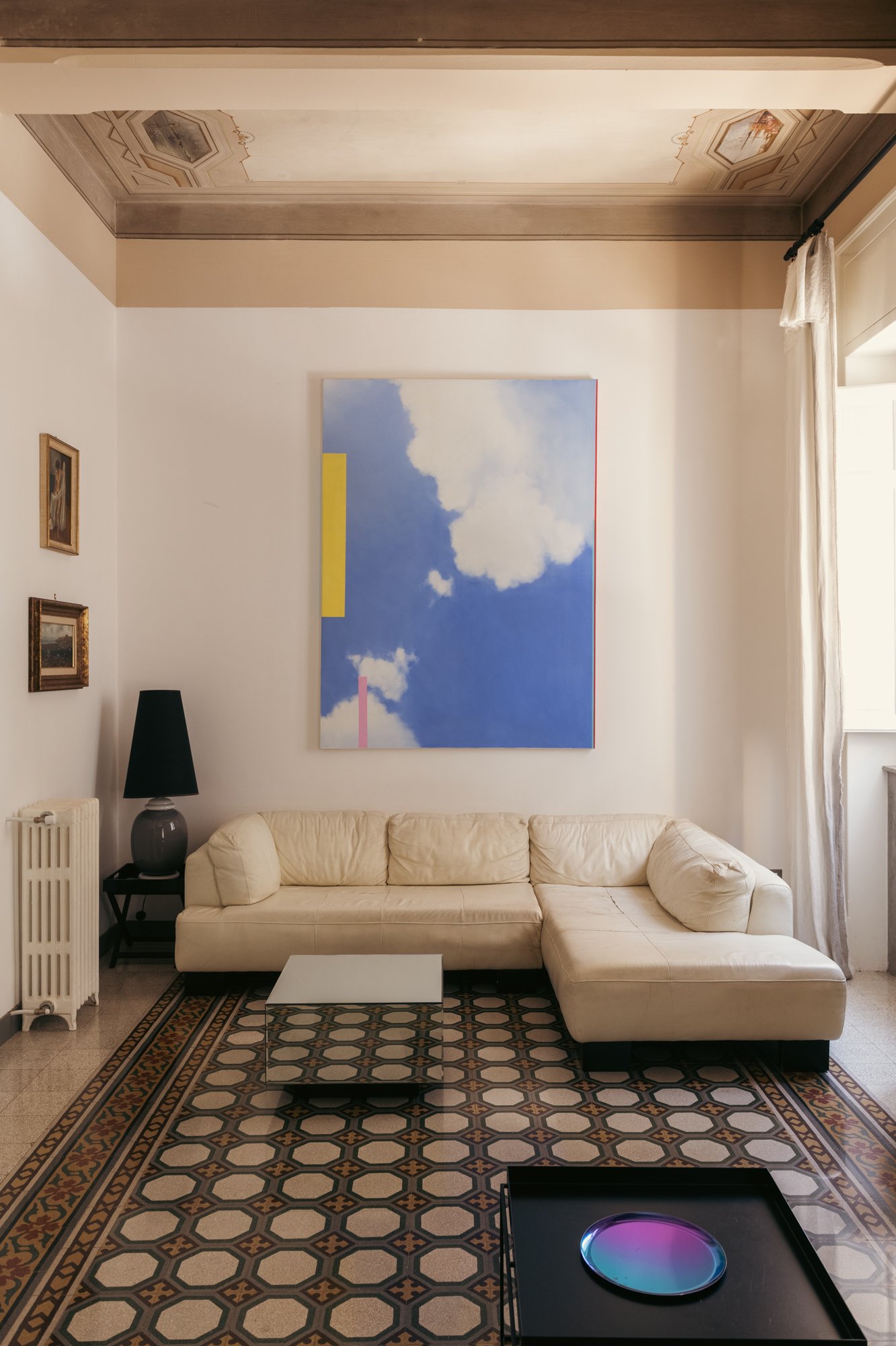 Nella zona living dell'appartamento a Palermo, pavimenti storici restaurati, soffitti decorati e opere d'arte contemporanea convivono in un equilibrio tra memoria e trasformazione.