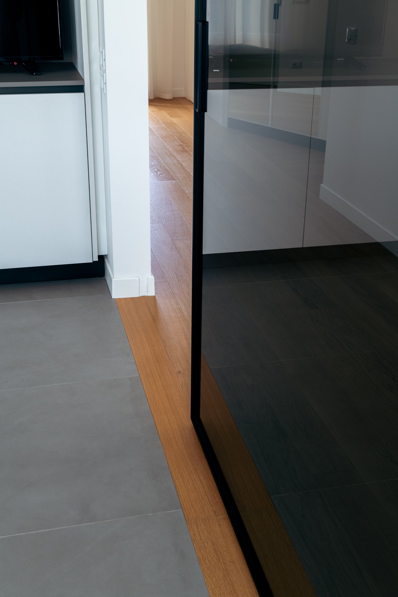Dettaglio della porta a vetri Rimadesio e del rapporto con le superfici in gres e parquet rovere.