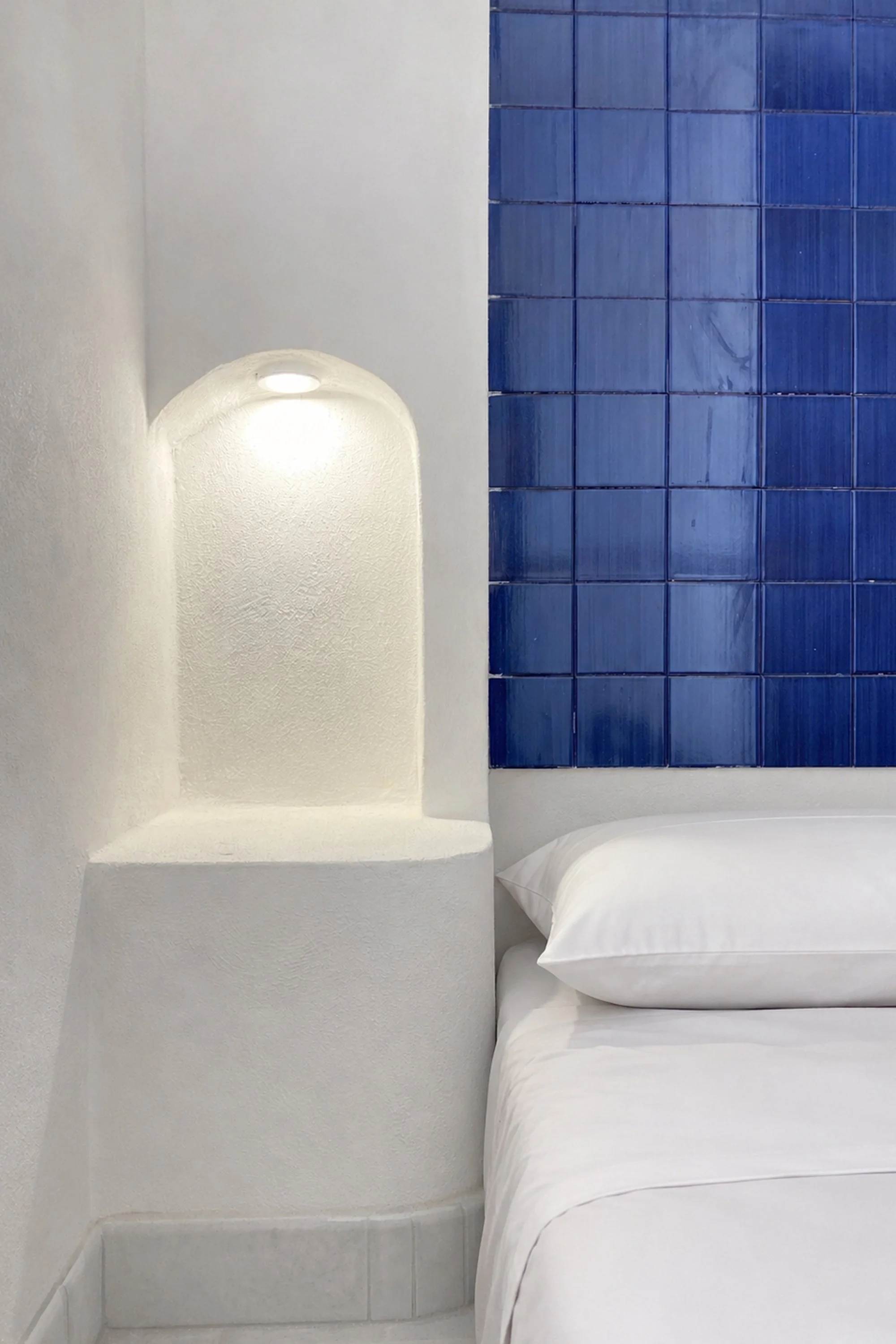 Dettaglio della camera da letto del progetto Lithos, recupero e ristrutturazione di un dammuso a Pantelleria. La nicchia illuminata emerge dalla massa muraria modellata attraverso superfici curve continue, reinterpretando l’architettura tradizionale 
