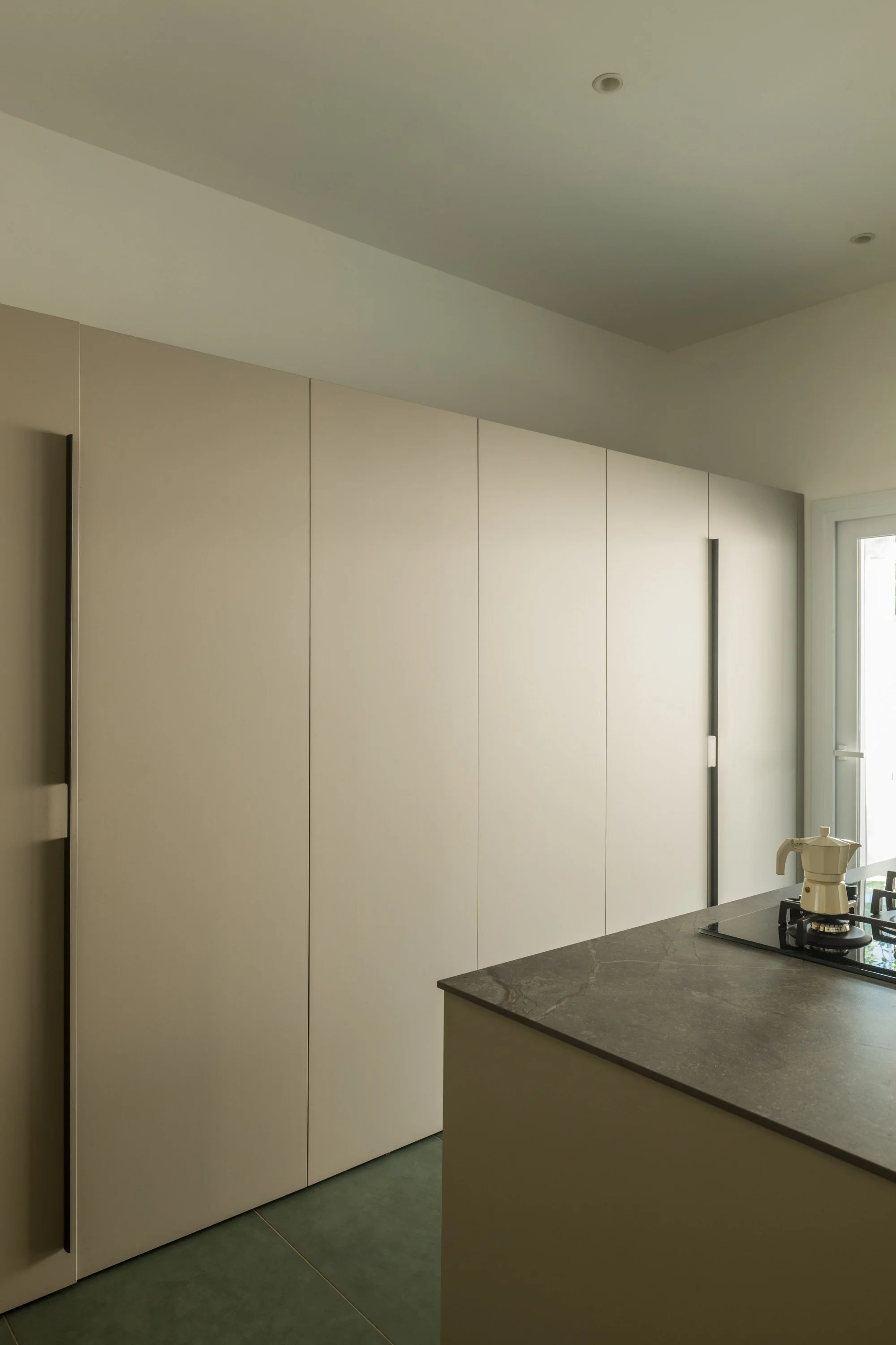 Cucina della villa ristrutturata a Mondello, Palermo, con il sistema contenitore chiuso che integra gli elementi funzionali nella parete e mantiene una superficie continua e minimale. Il progetto di FDR Architetto utilizza l’apertura e la chiusura de