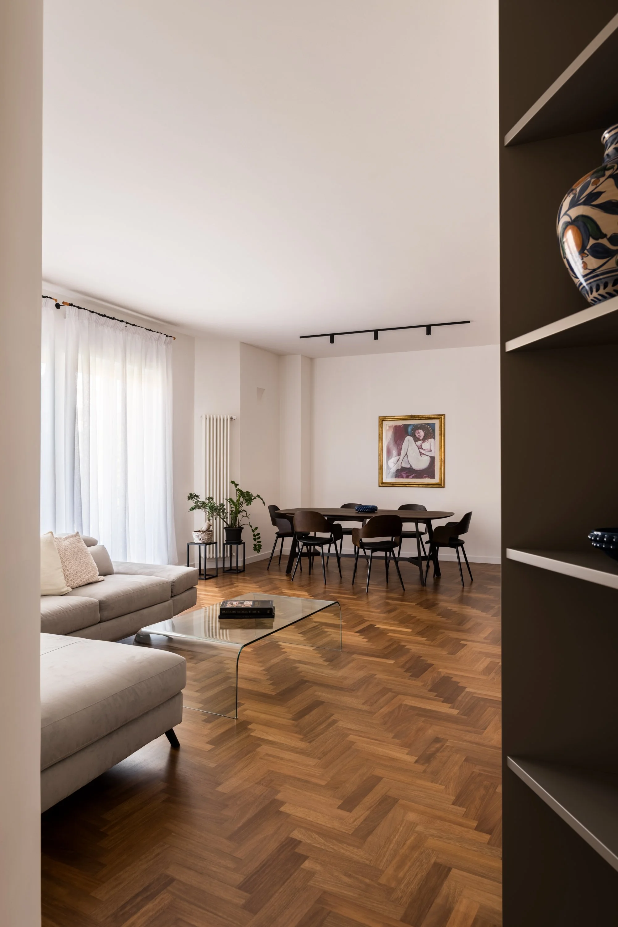 Vista del soggiorno e della zona pranzo con parquet in iroko a spina, illuminazione naturale e continuità spaziale tra gli ambienti.