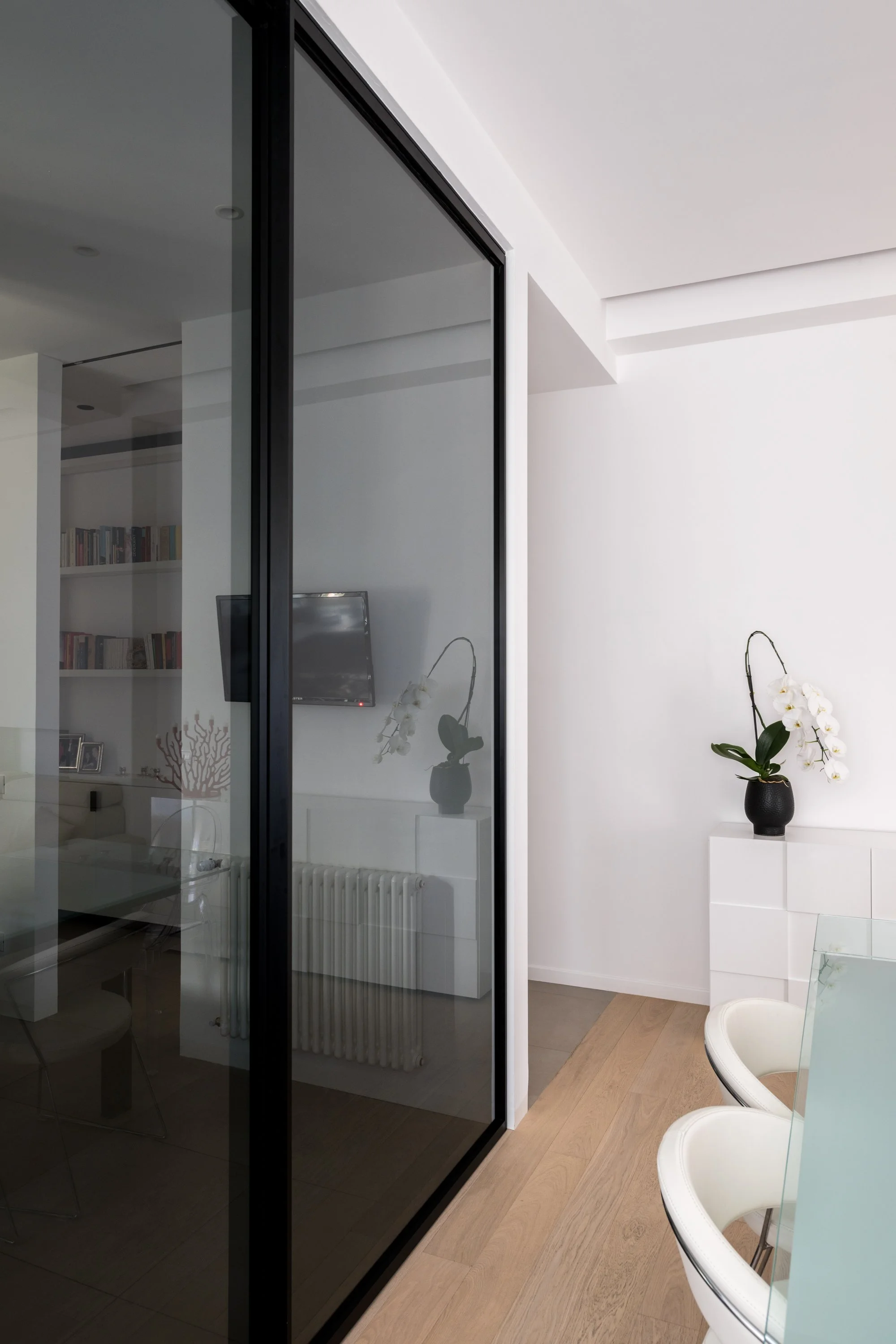 Porta vetrata fumé scorrevole in un appartamento ristrutturato a Palermo. Il diaframma trasparente filtra la luce e le visuali tra gli ambienti, costruendo una relazione dinamica tra connessione e privacy attraverso un sistema di soglie mobili.