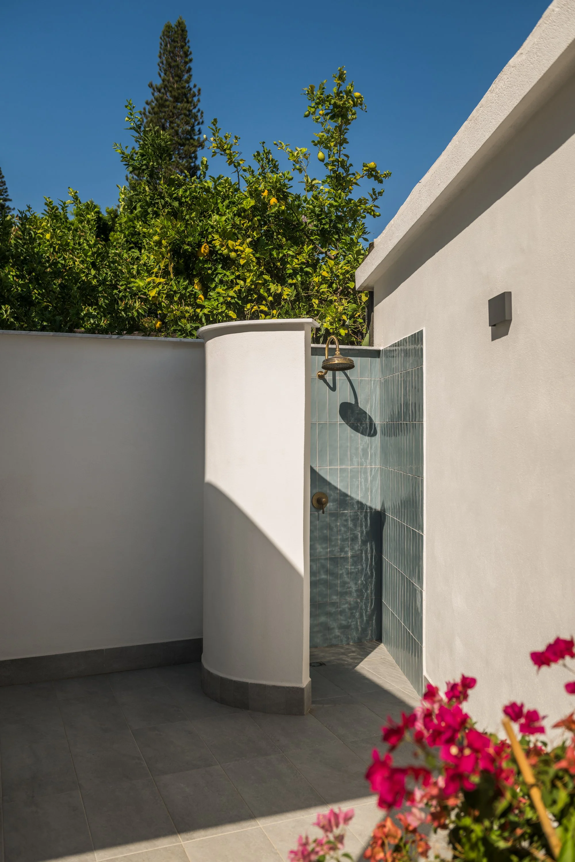 Doccia esterna progettata nella nuova area outdoor della villa ristrutturata a Mondello, Palermo. La superficie in piastrelle ceramiche verdi dialoga con le pareti bianche, la pavimentazione e la vegetazione del giardino mediterraneo. Il progetto com
