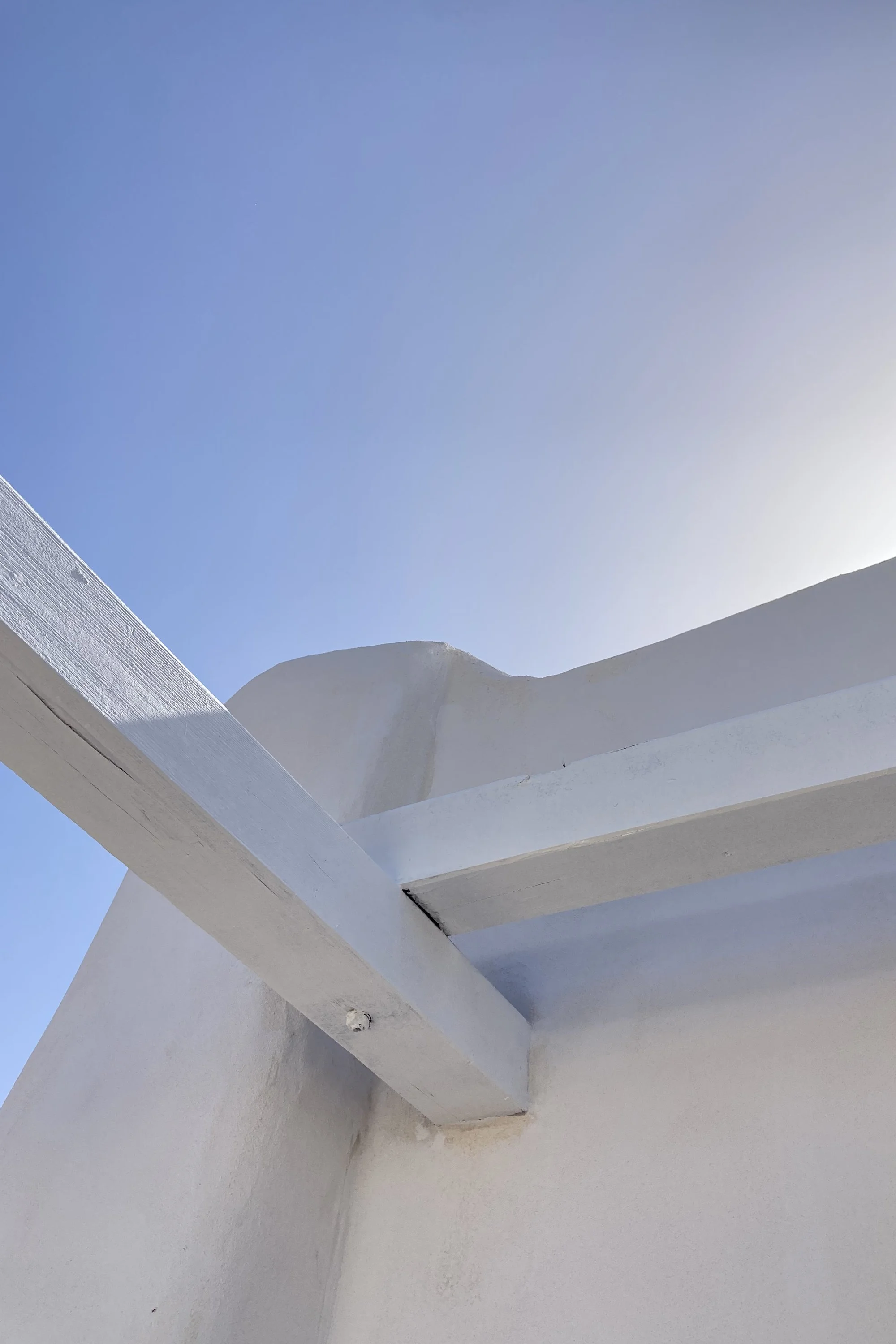 Dettaglio della curvatura del prospetto di un dammuso ristrutturato a Pantelleria con pergolato bianco e cielo mediterraneo.