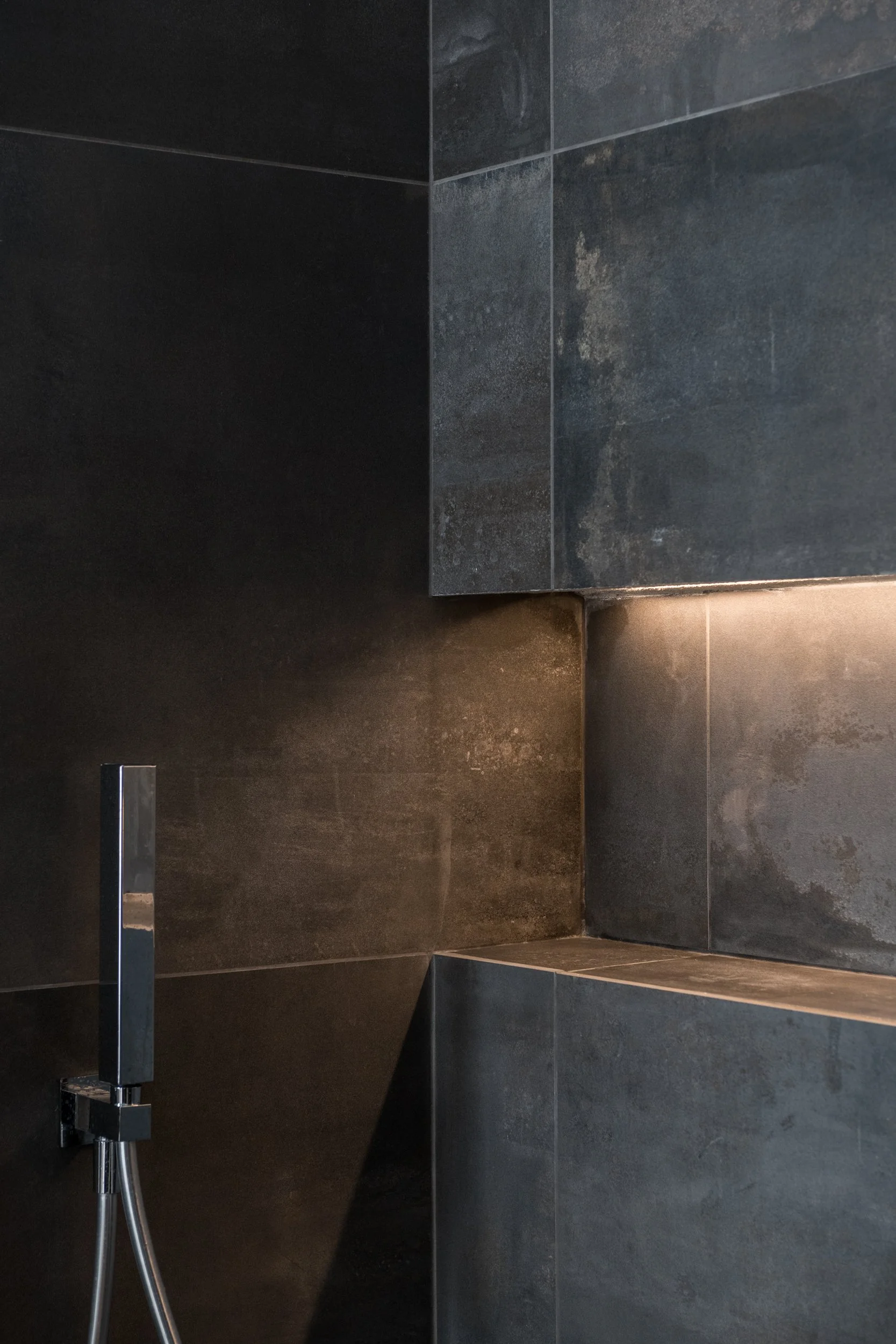 Un taglio di luce attraversa una superficie materica continua, trasformando il bagno in una composizione di ombre, riflessi e profondità.