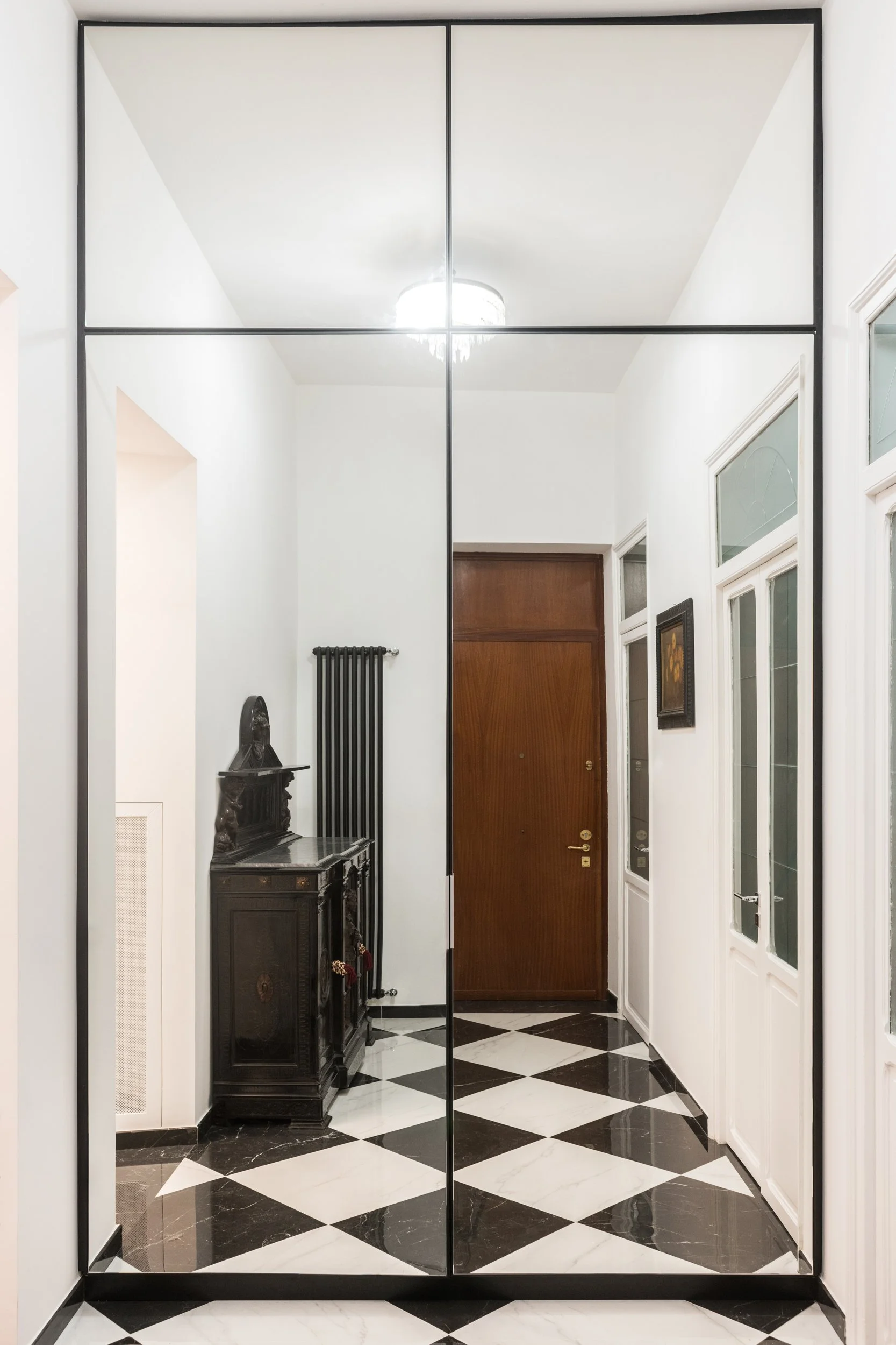Armadio ad ante specchiate nell'ingresso di un appartamento ristrutturato a Palermo con pavimento in gres porcellanato effetto marmo bianco e nero e mobili antichi restaurati. Foto dell'ingresso del progetto Dinamo, intervento di ristrutturazione e r