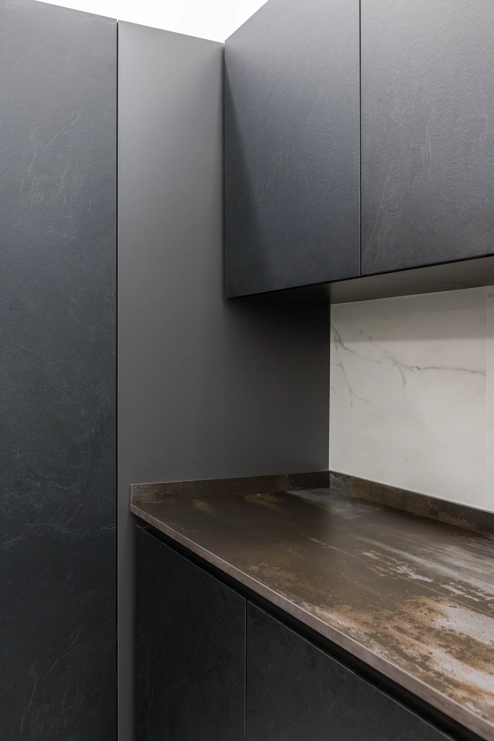 Dettaglio della cucina realizzata nel progetto Dinamo a Palermo. Le basi e i pensili con finitura effetto pietra si combinano con il rivestimento in gres porcellanato effetto marmo e con il piano di lavoro dalle tonalità scure. L'isola centrale diven