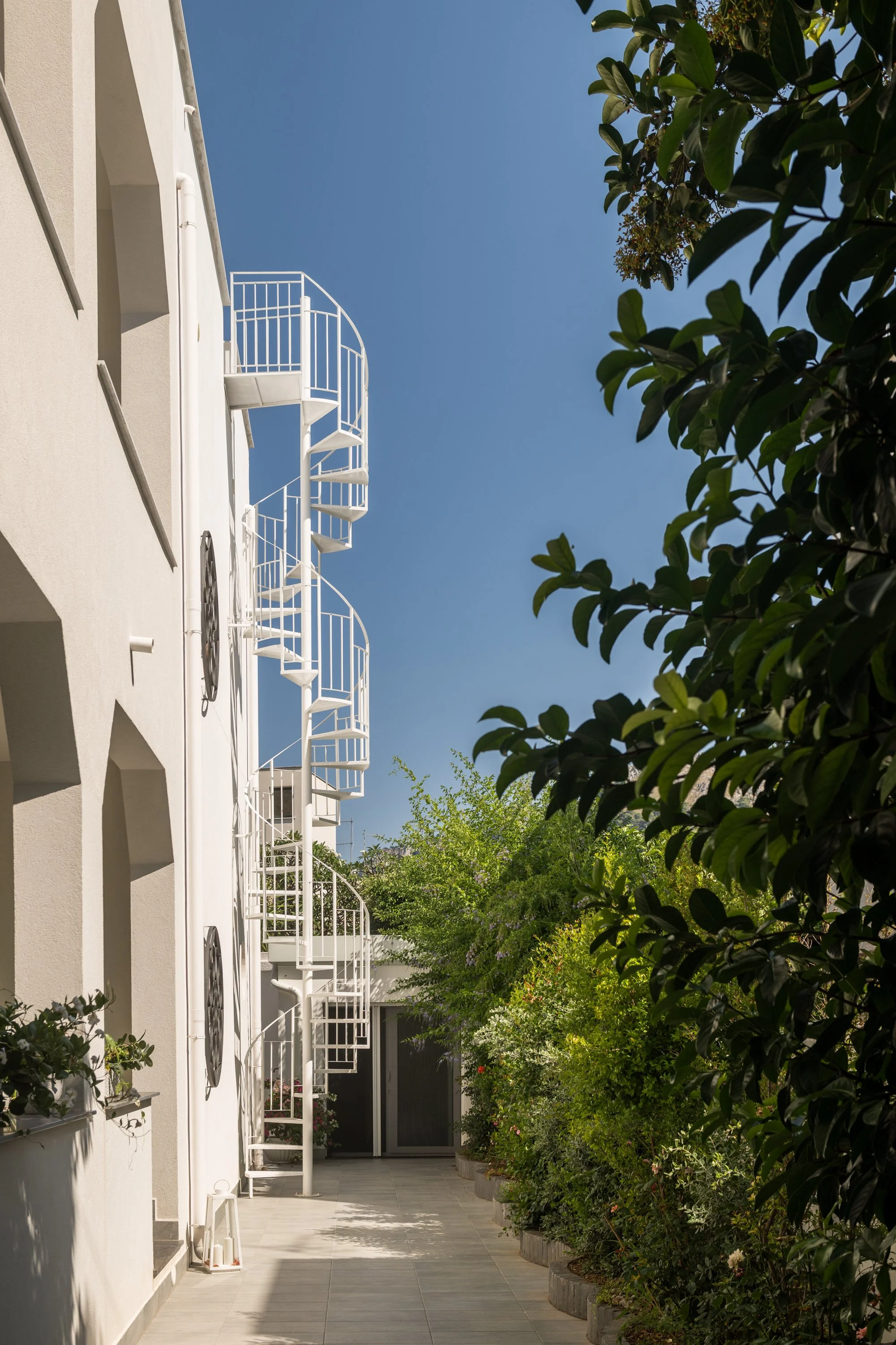 Ristrutturazione e frazionamento di una villa unifamiliare a Mondello, Palermo. Progetto e direzione lavori di Francesco Di Raimondo fondatore dello studio FDR Architetto. Il prospetto bianco della villa è affiancato dalla scala esterna che collega l
