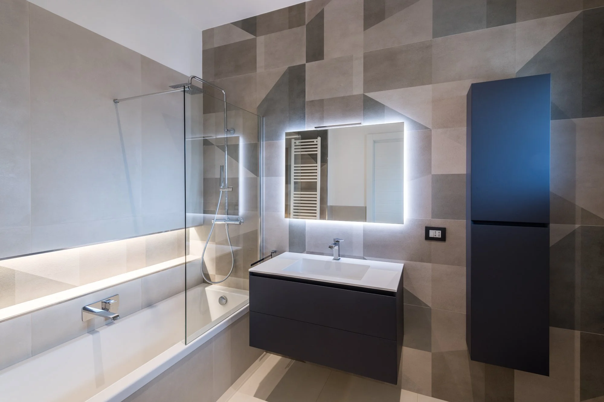 Il bagno padronale del progetto Mikado a Palermo è caratterizzato da una composizione geometrica in gres Marazzi che costruisce una trama di superfici e direzioni. Vasca, illuminazione integrata e arredi sospesi definiscono uno spazio equilibrato tra