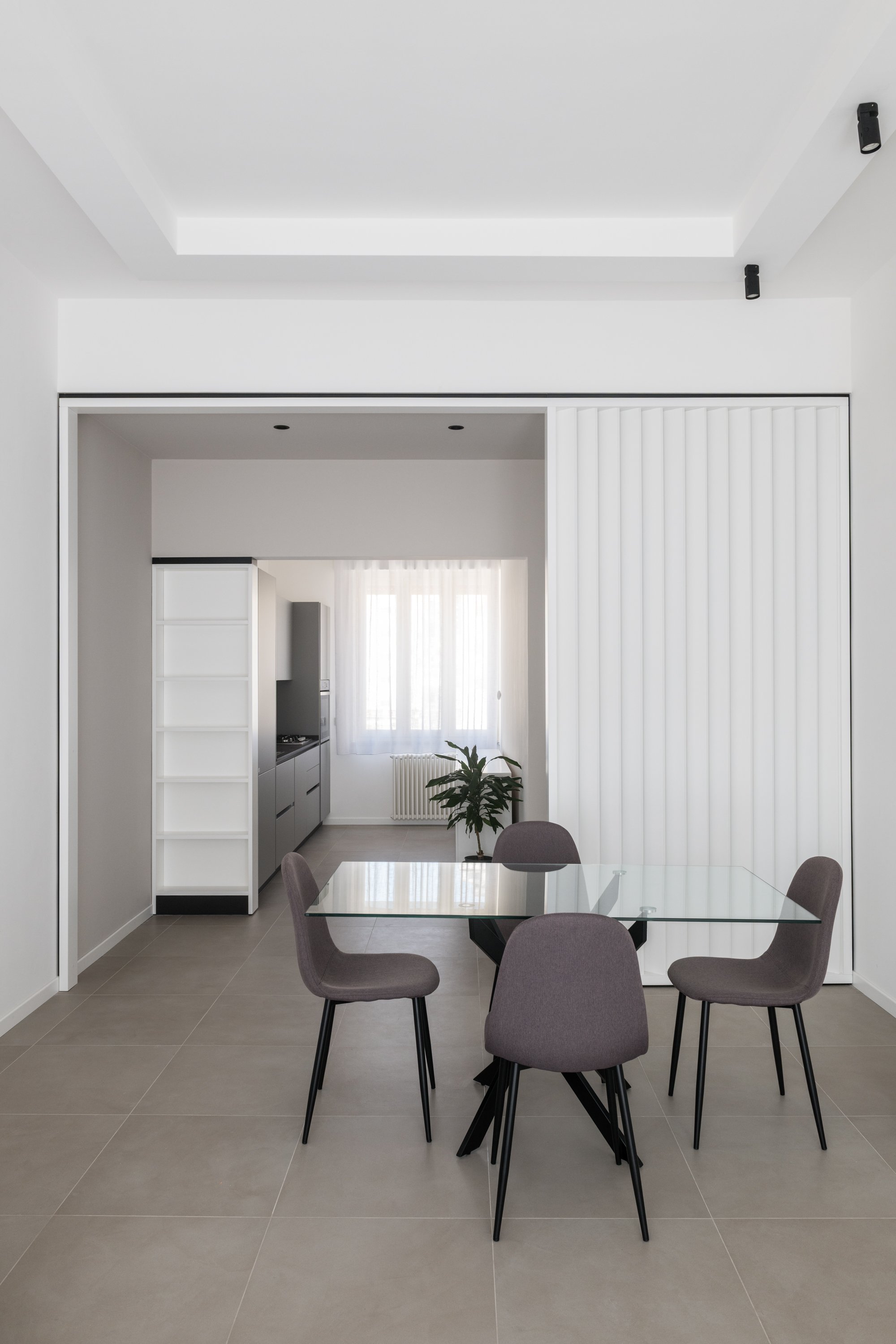 La zona pranzo dell’appartamento Ink si sviluppa in continuità con la cucina attraverso un sistema di connessioni visive e spaziali. Il brise-soleil bianco filtra gli ambienti mentre il gres continuo Marazzi e le superfici monocromatiche rafforzano l