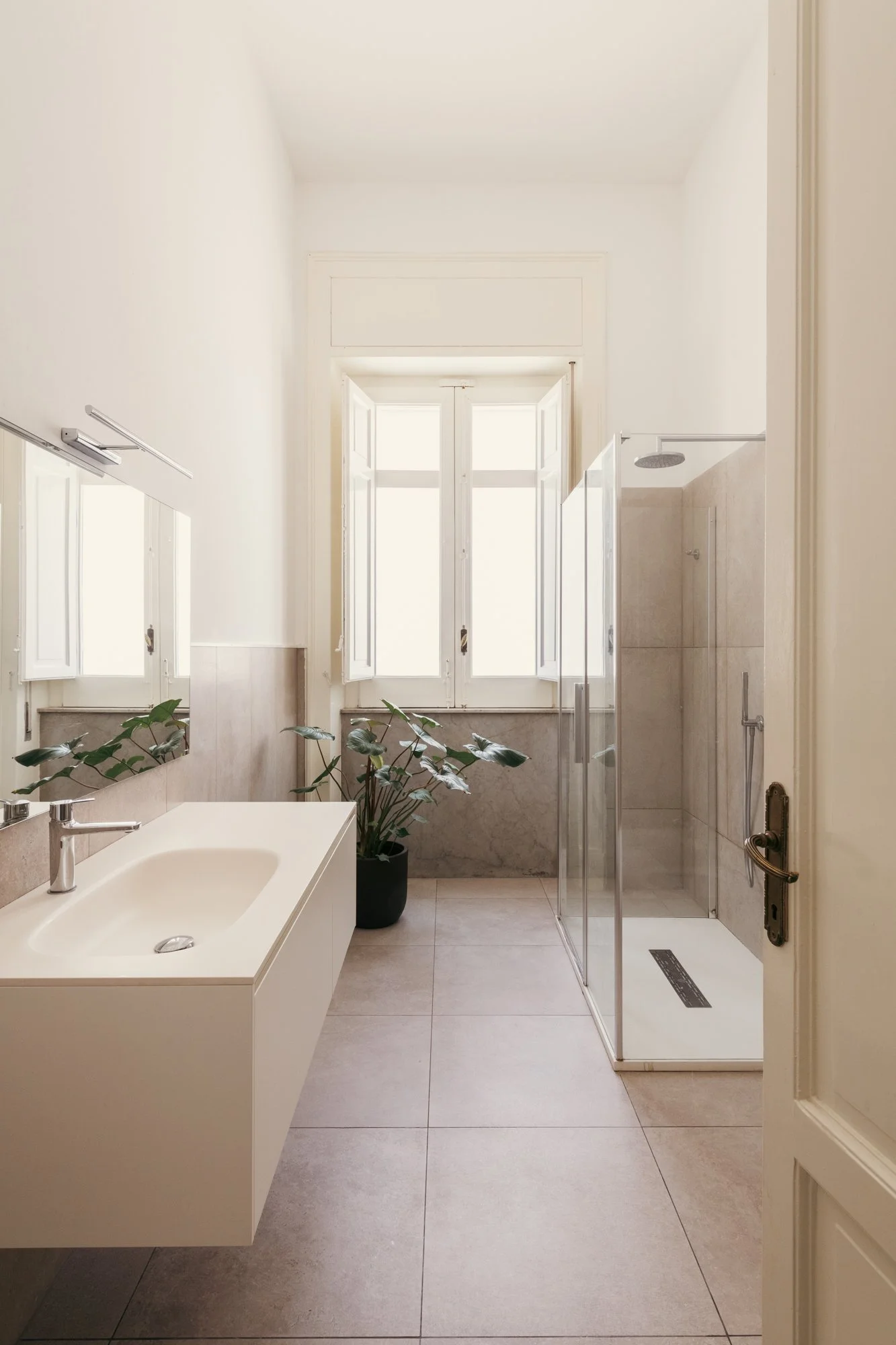 Materiali neutri, lavabo Antonio Lupi e rubinetteria Fantini definiscono il bagno dell'appartamento restaurato a Palermo, in continuità con il dialogo tra memoria e contemporaneità che caratterizza il progetto.