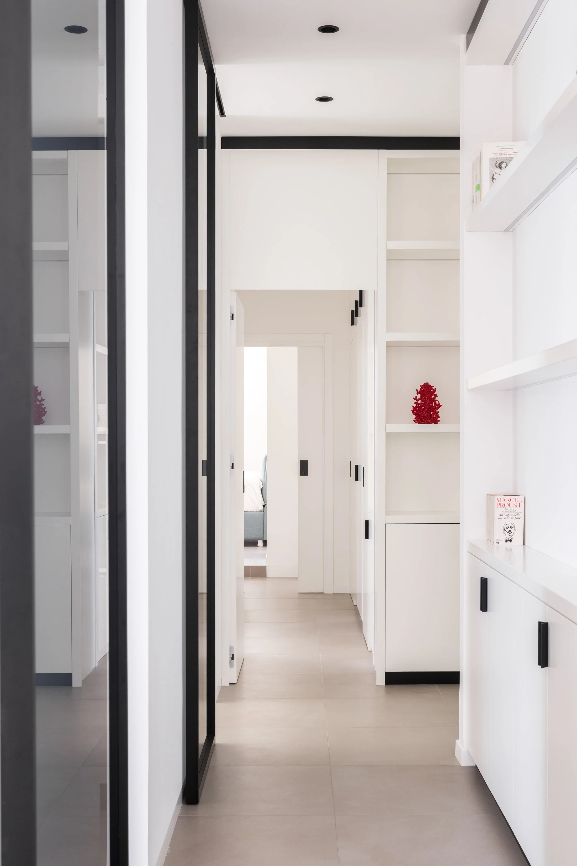 Questa immagine evidenzia uno dei dispositivi fondamentali di Slide: la capacità della falegnameria di diventare architettura. Il corridoio non è definito da pareti e porte autonome, ma da una struttura continua che incorpora funzioni differenti all'