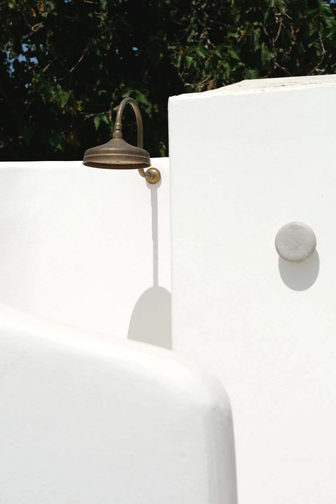 Doccia esterna della villa S/Tone a Ustica. Volumi intonacati bianchi, dettagli in ottone e luce mediterranea definiscono uno spazio essenziale dove architettura, materia e paesaggio si fondono in un'esperienza all'aperto.
