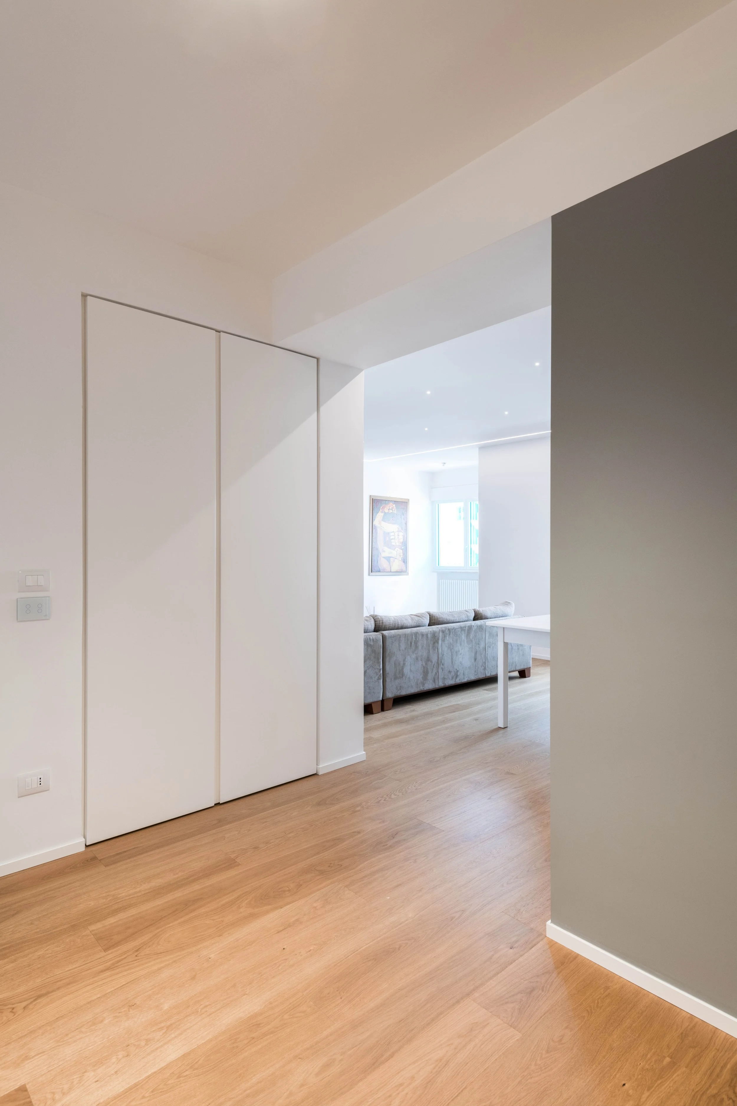 Il volume centrale grigio definisce le gerarchie spaziali e organizza i percorsi tra ingresso, soggiorno e studio. La ristrutturazione dell’appartamento Mikado a Palermo valorizza luce naturale, parquet in rovere e continuità visiva attraverso una nu
