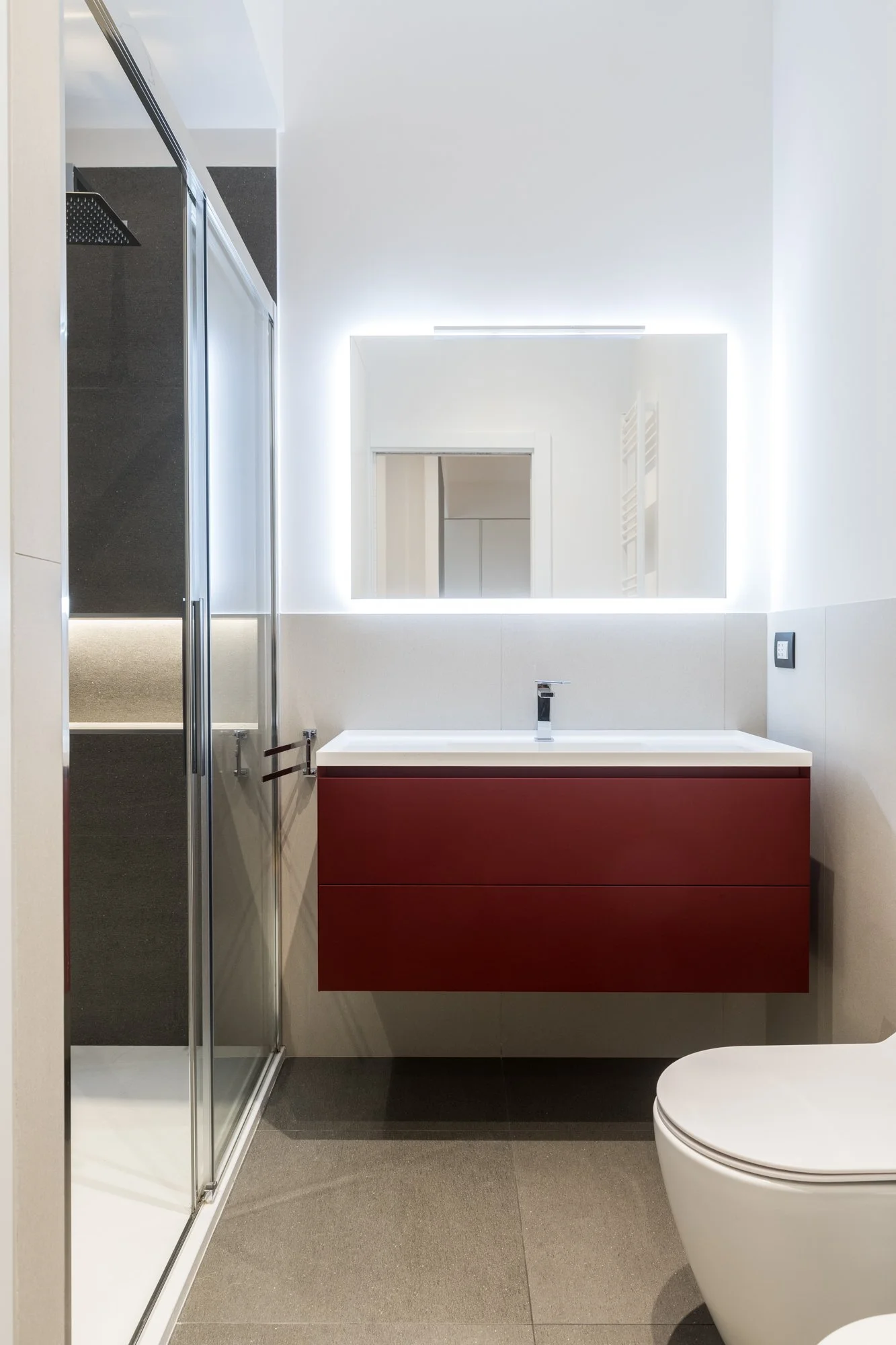 Il bagno di servizio del progetto Mikado a Palermo è caratterizzato dal contrasto tra superfici neutre e il volume sospeso rosso del lavabo. Luce integrata, materiali essenziali e dettagli contemporanei definiscono uno spazio ordinato e funzionale.