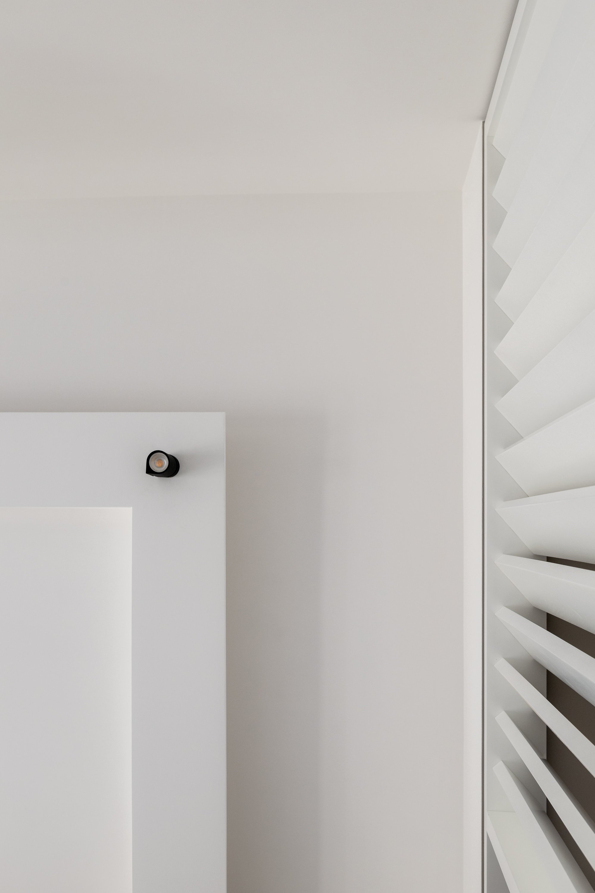 Dettaglio del brise-soleil laccato bianco progettato come elemento filtro tra gli ambienti della zona giorno. Le lame verticali definiscono una soglia permeabile che mantiene la continuità visiva e valorizza la luce naturale all’interno dell’appartam