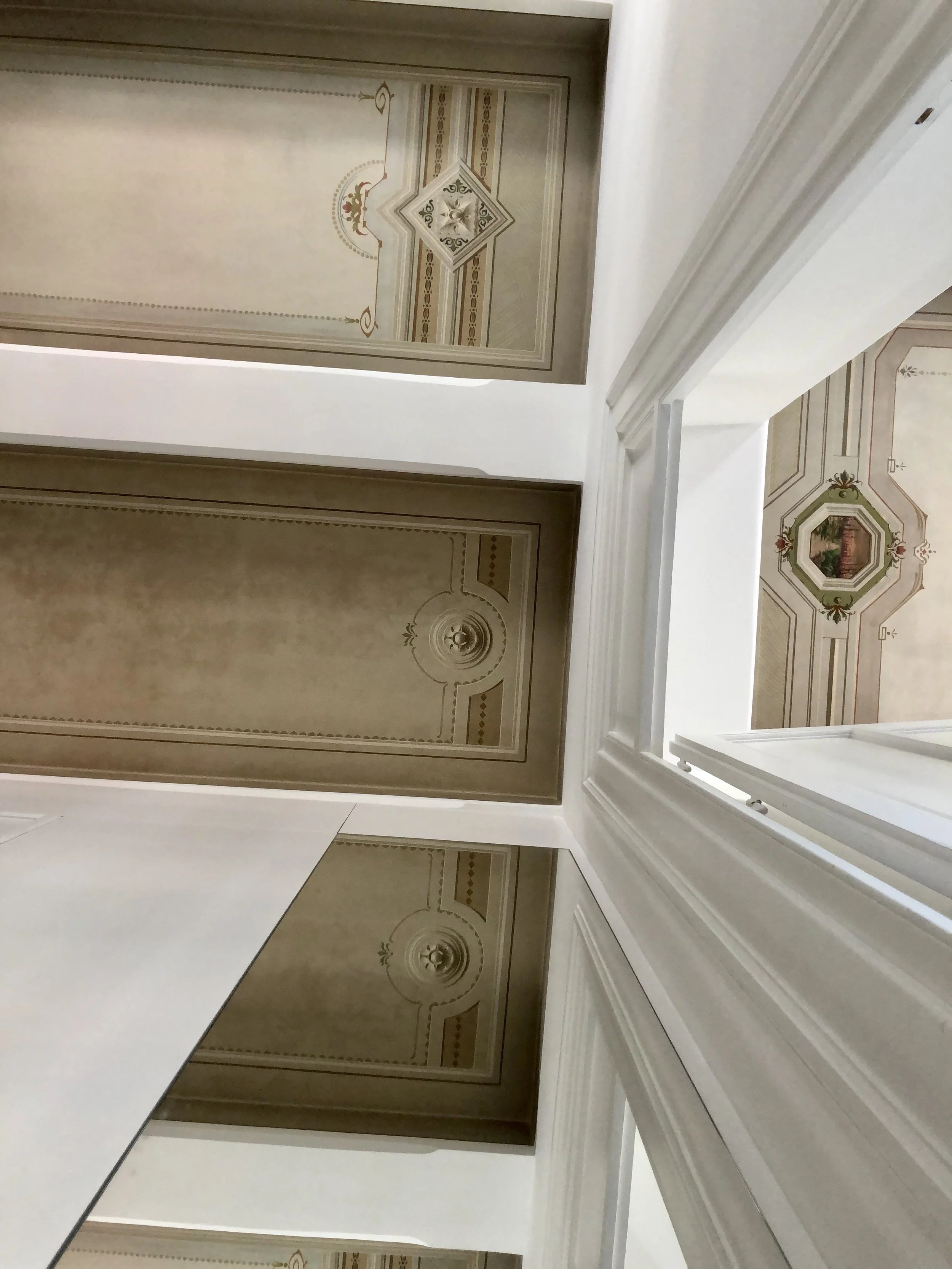 Dettaglio della porta a specchio integrata nella boiserie contemporanea di un appartamento storico restaurato a Palermo. La superficie riflettente amplifica la profondità dello spazio e moltiplica la percezione dei soffitti dipinti originali restaura