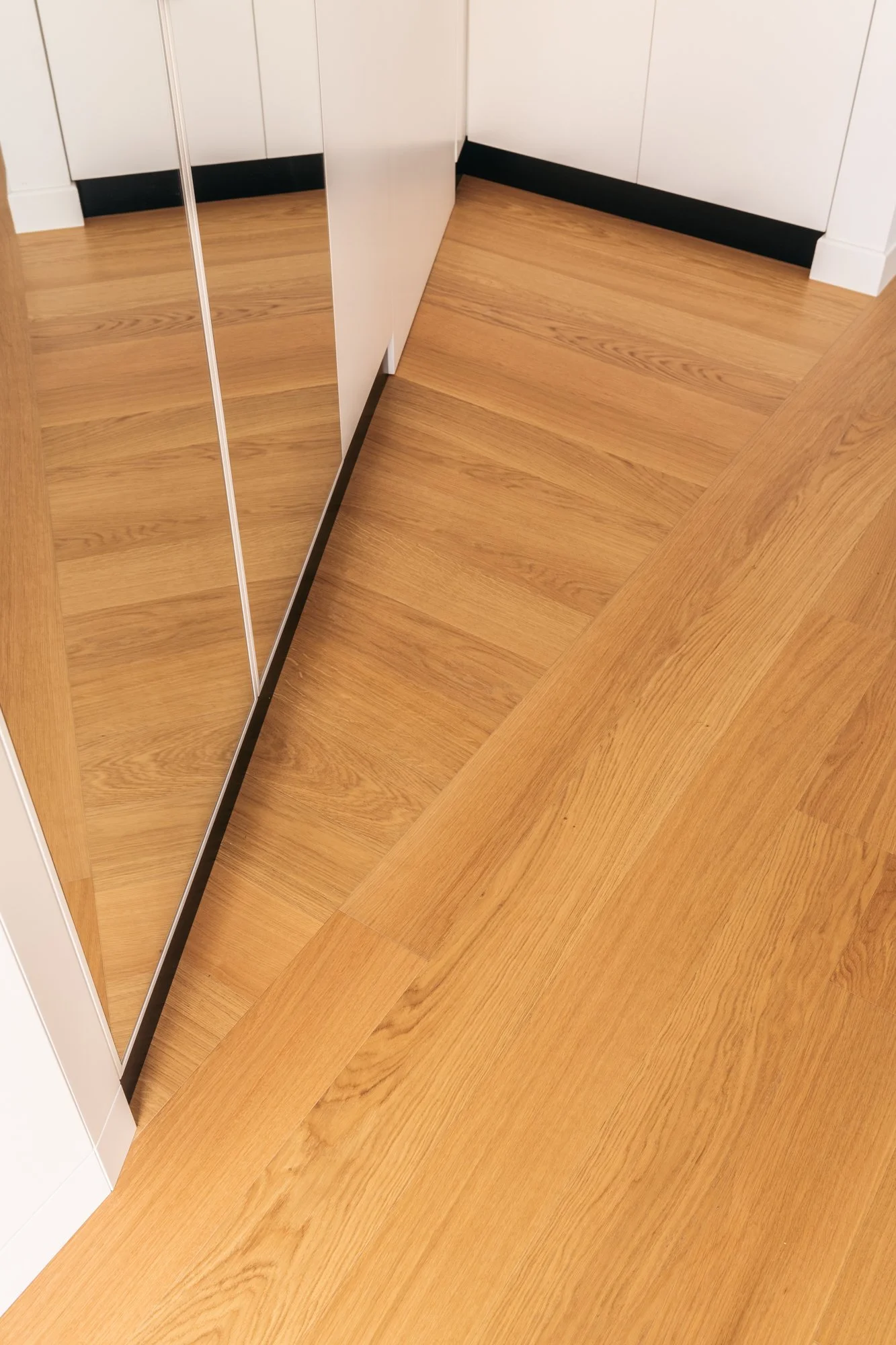 Il riflesso delle superfici amplifica la continuità del parquet in rovere, valorizzando la percezione dello spazio nell'appartamento ristrutturato a Palermo.