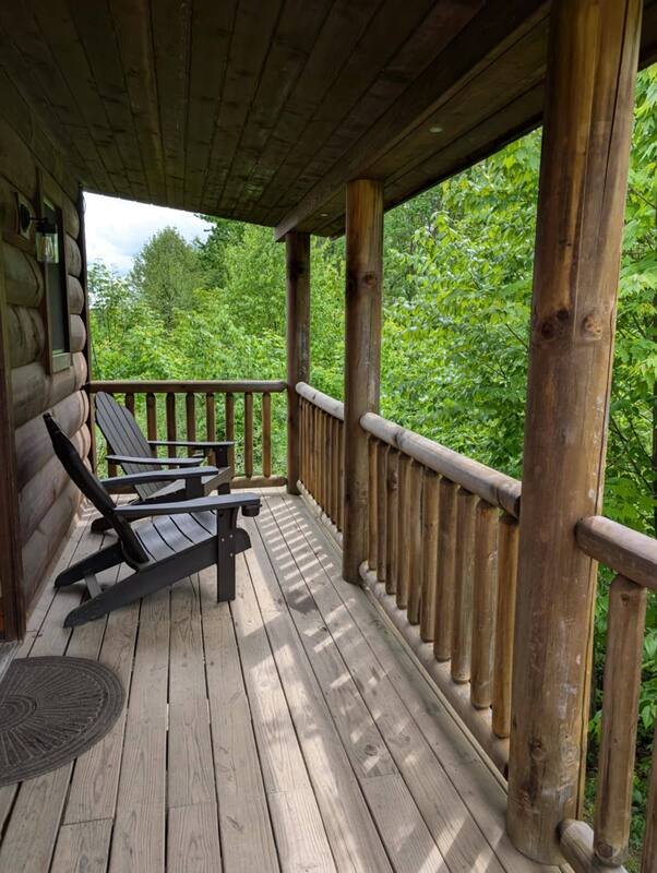 A wooden porch with two black Adirondack chairs overlooking green trees.