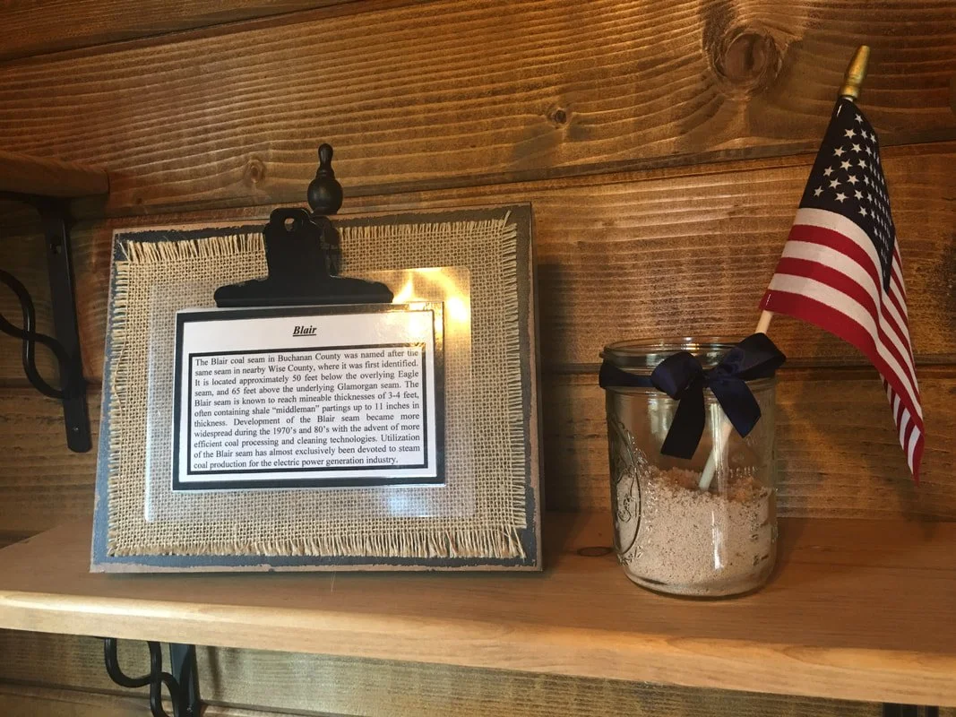Information plaque about the Blair coal seam, next to a small American flag in a glass jar filled with sand, on a wooden shelf.